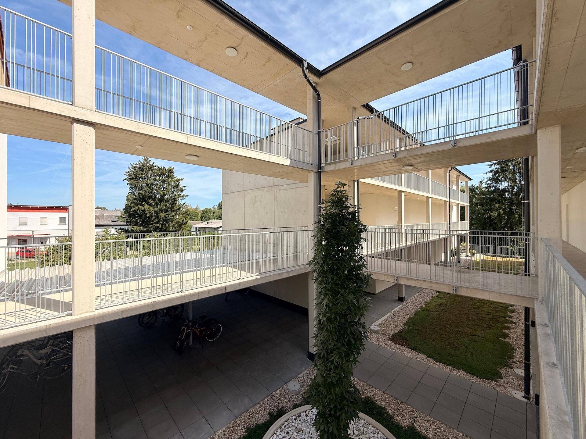 Weitläufiger Blick über den Innenhof eines modernen Wohnkomplexes mit Grünflächen und Fahrradabstellplatz.
