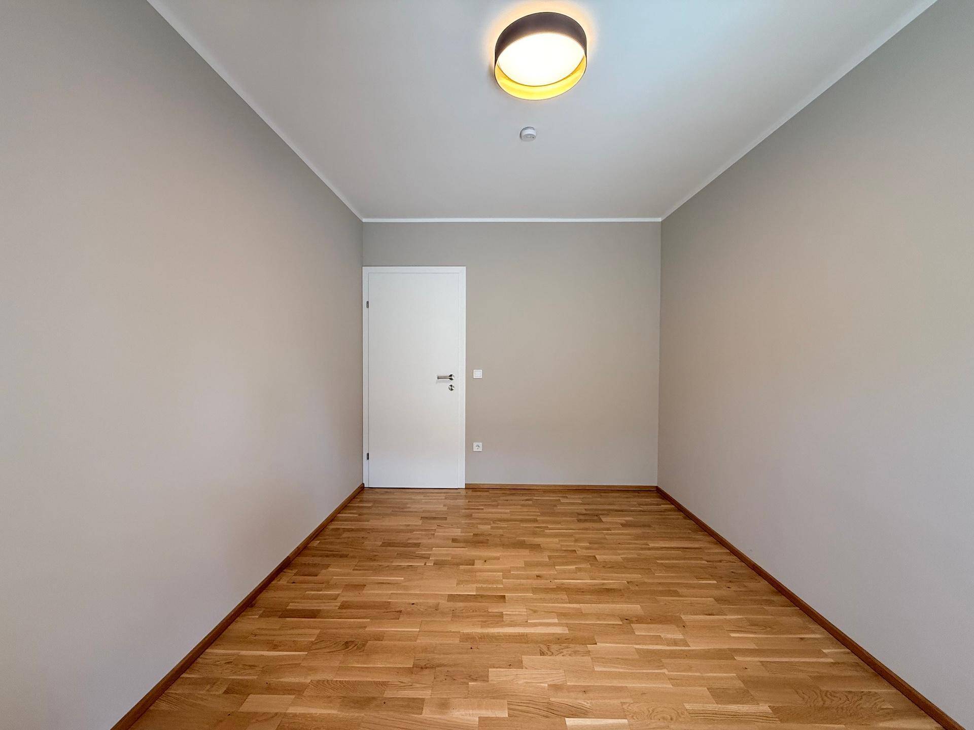 Heller Raum mit hellgrauen Wänden und Holzboden, bereit zur individuellen Gestaltung.