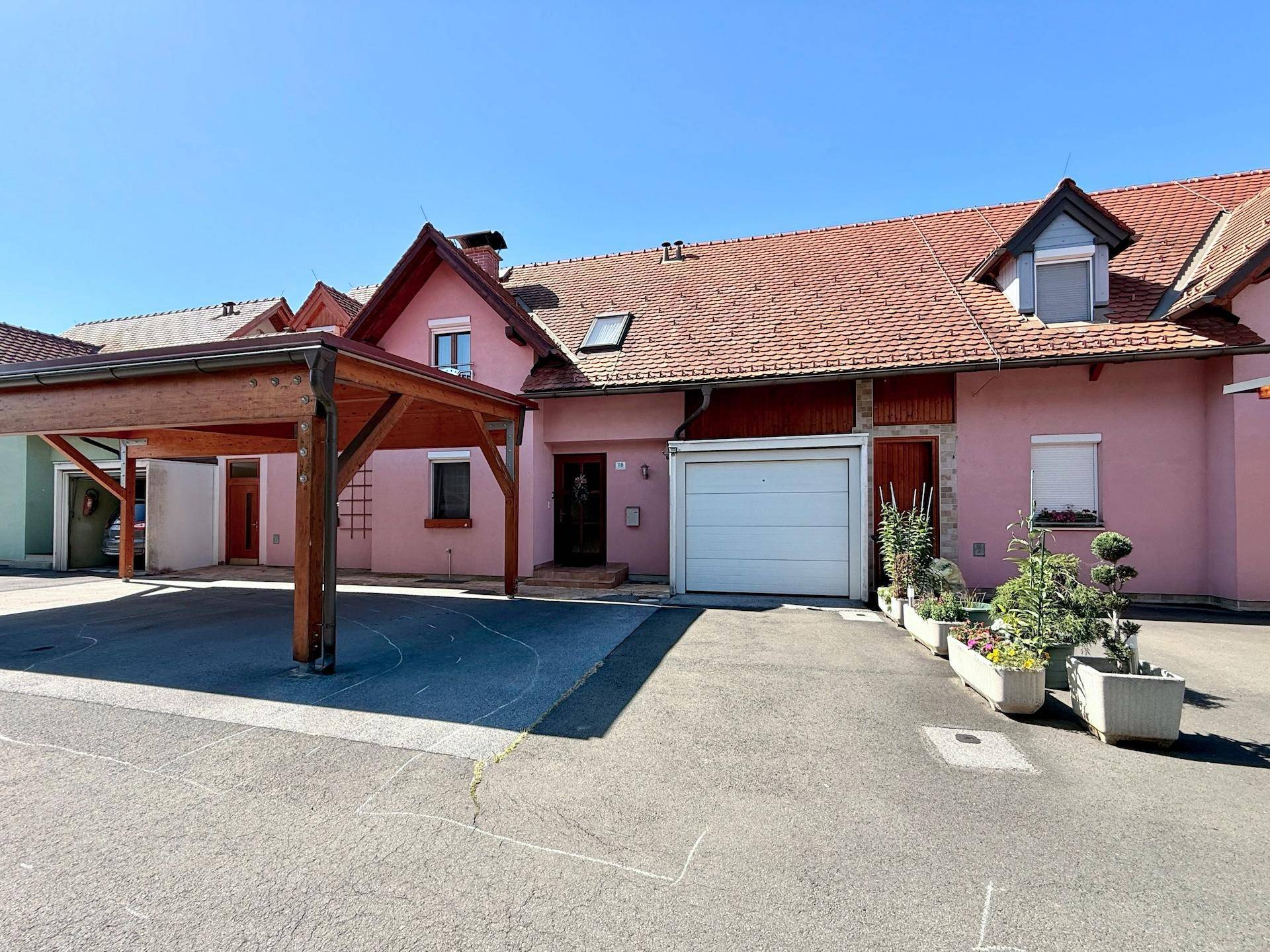 Hausfassade mit integriertem Carport und Garagentor, umgeben von gepflegten Blumenkästen.