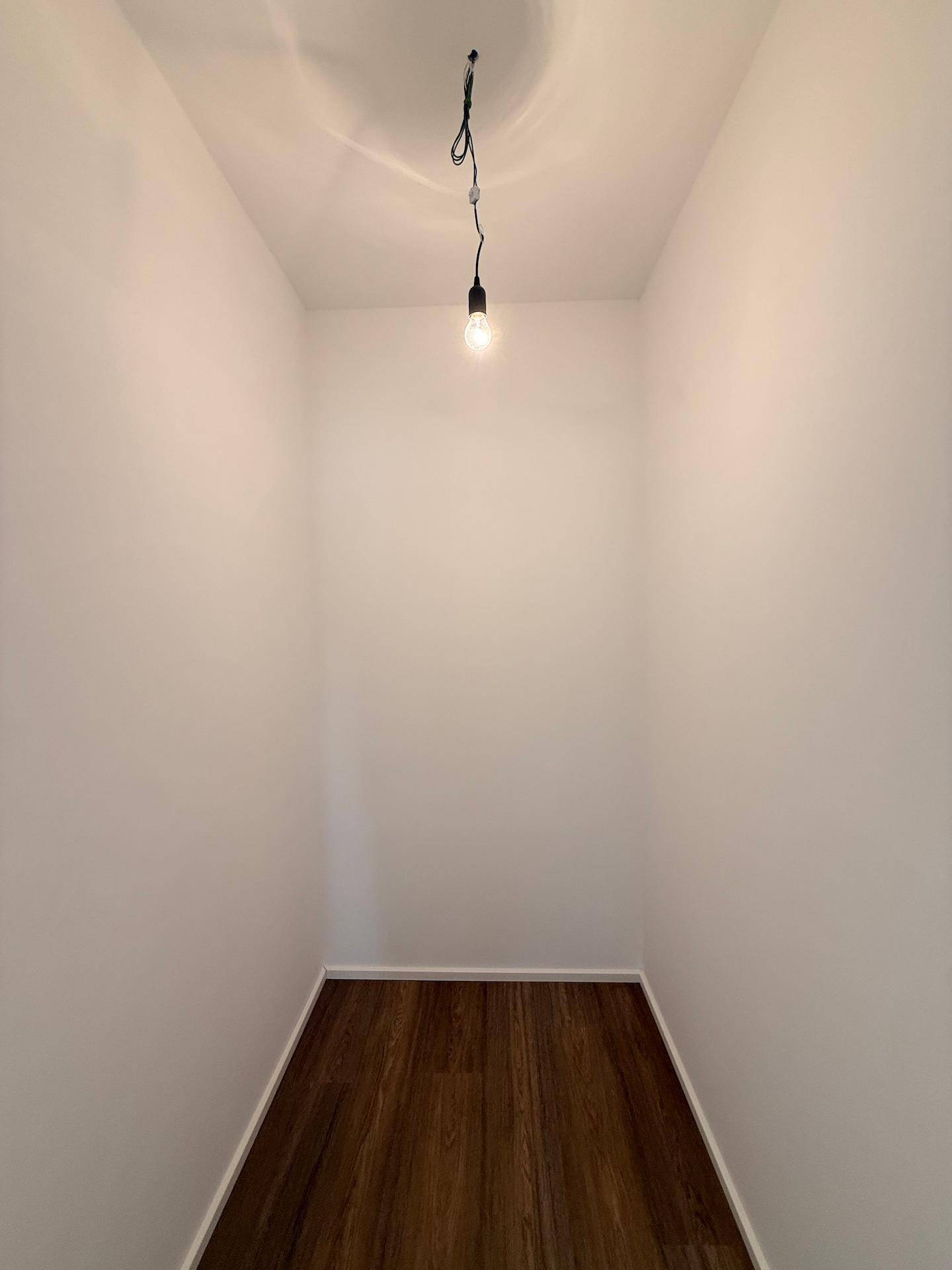 Kleiner, leerer Abstellraum mit dunklem Holzfußboden, ideal für zusätzlichen Stauraum.