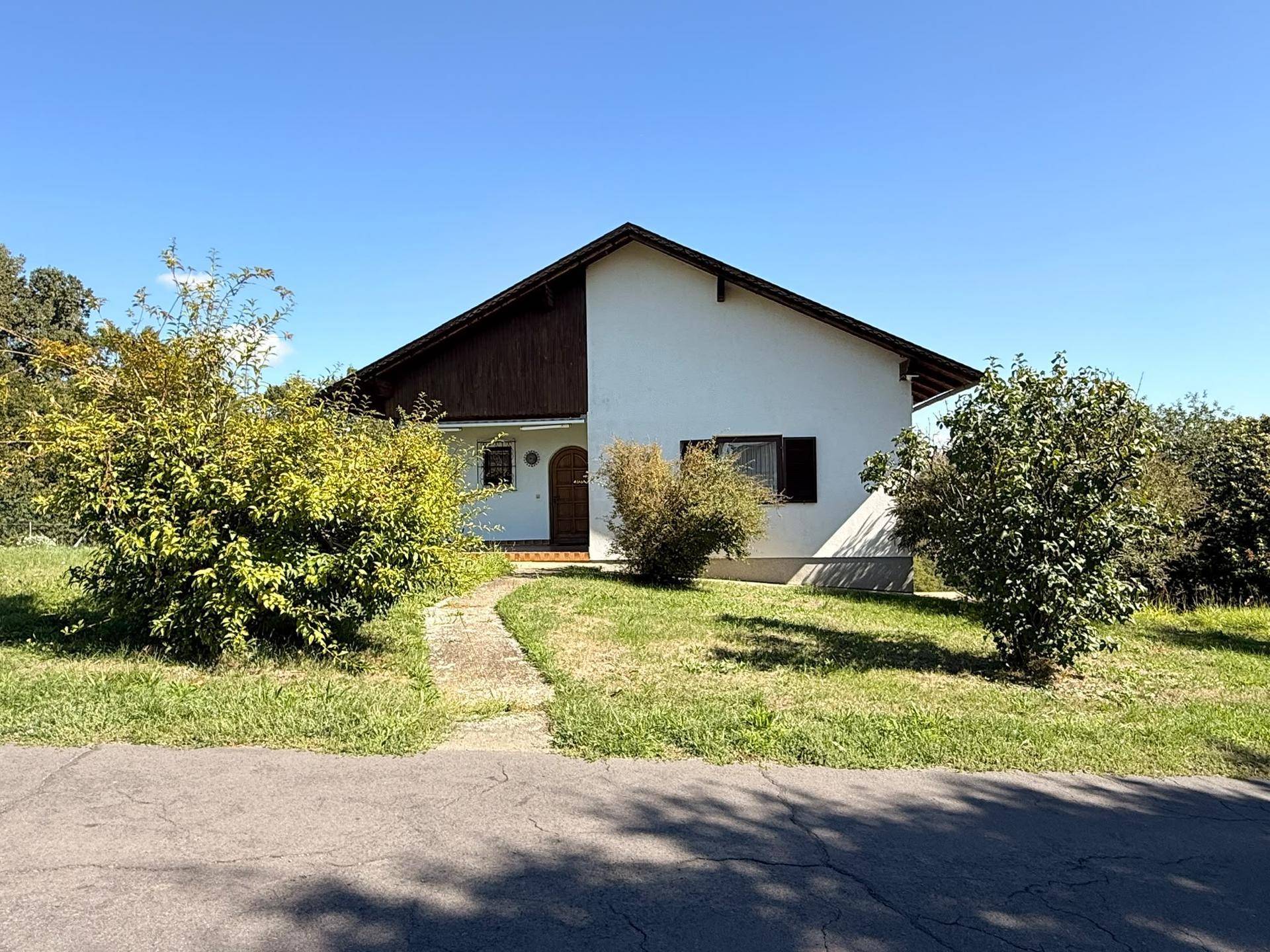 Vorderansicht des Einfamilienhauses mit Vorgarten und Zugangsweg unter strahlend blauem Himmel.