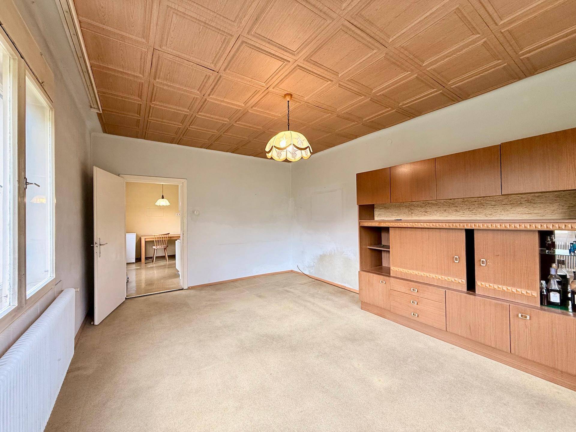 Geräumiges Wohnzimmer mit Holzdecke, Teppichboden und großem Einbauschrank, bietet viel Platz.