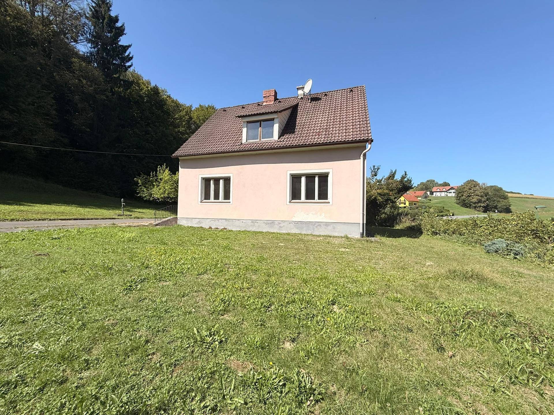 Rückansicht des Einfamilienhauses mit gepflegtem Rasen und Blick auf die umliegende Hügellandschaft.