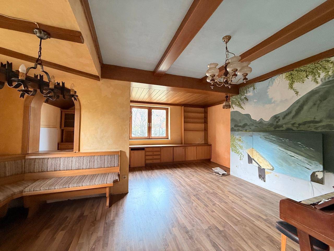 Gemütliches Wohnzimmer mit Holzbalken, Wandmalerei und eingebauter Sitzbank im alpinen Stil.