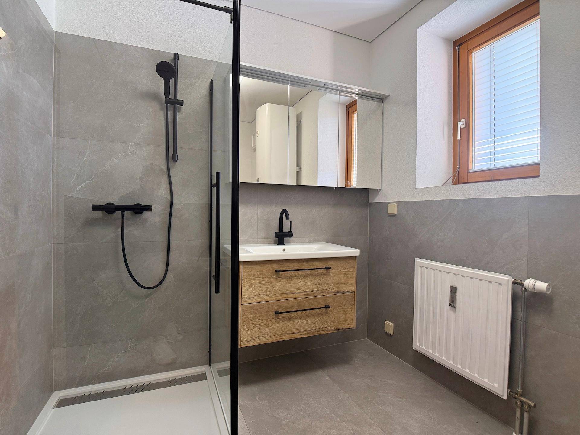 Stilvolles Badezimmer mit ebenerdiger Dusche, modernem Waschtisch und Fenster für Tageslicht.