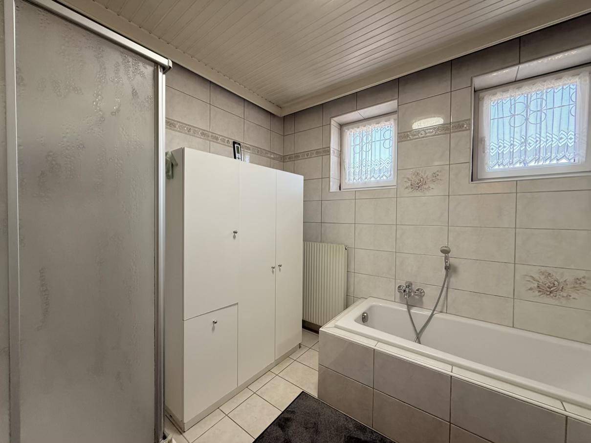 Gefliestes Badezimmer mit Badewanne, Duschkabine und Spiegelschrank, hell durch Fenster.
