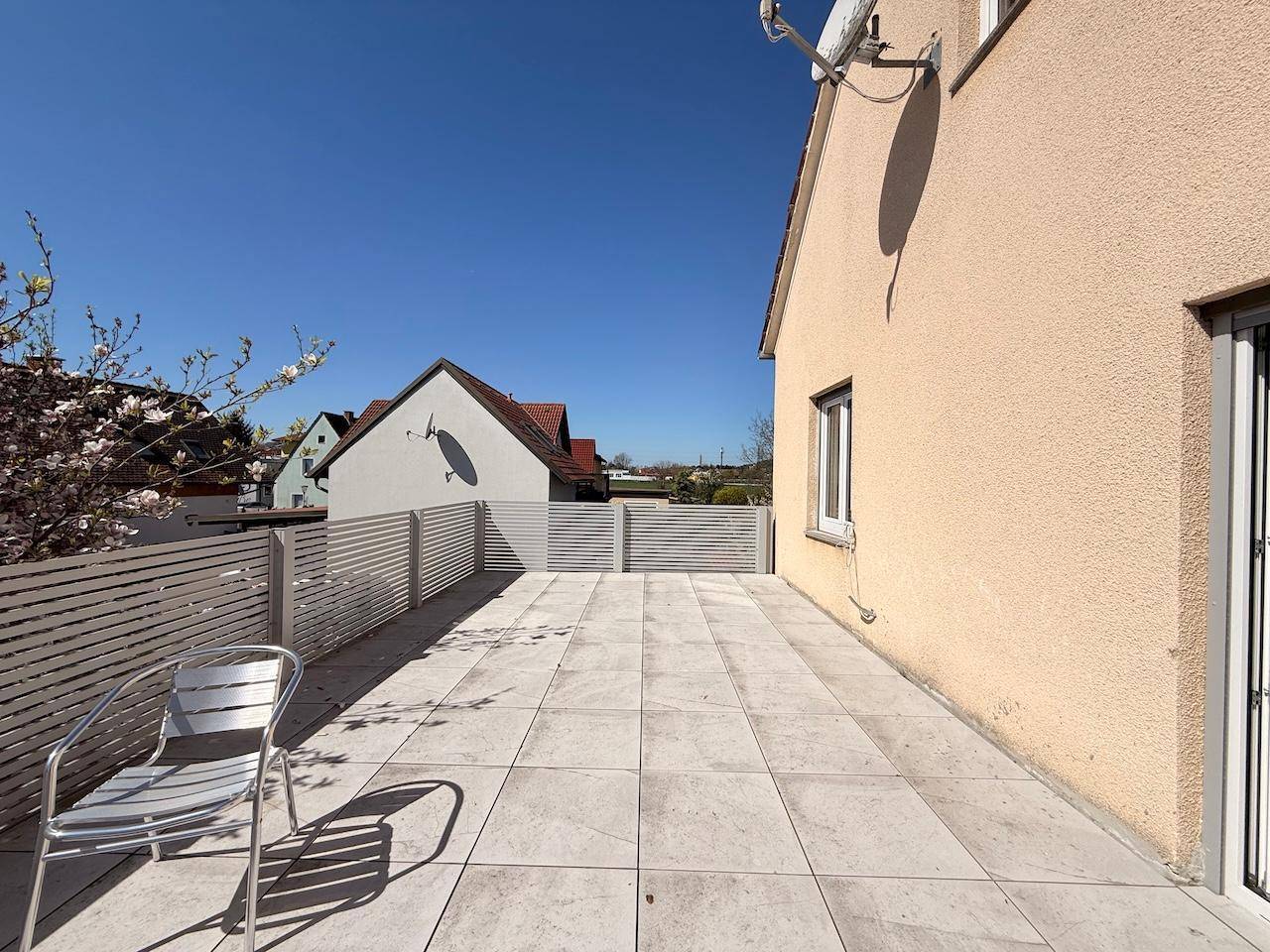 Große geflieste Terrasse mit Zaun und Sitzgelegenheit, ideal für sonnige Tage.