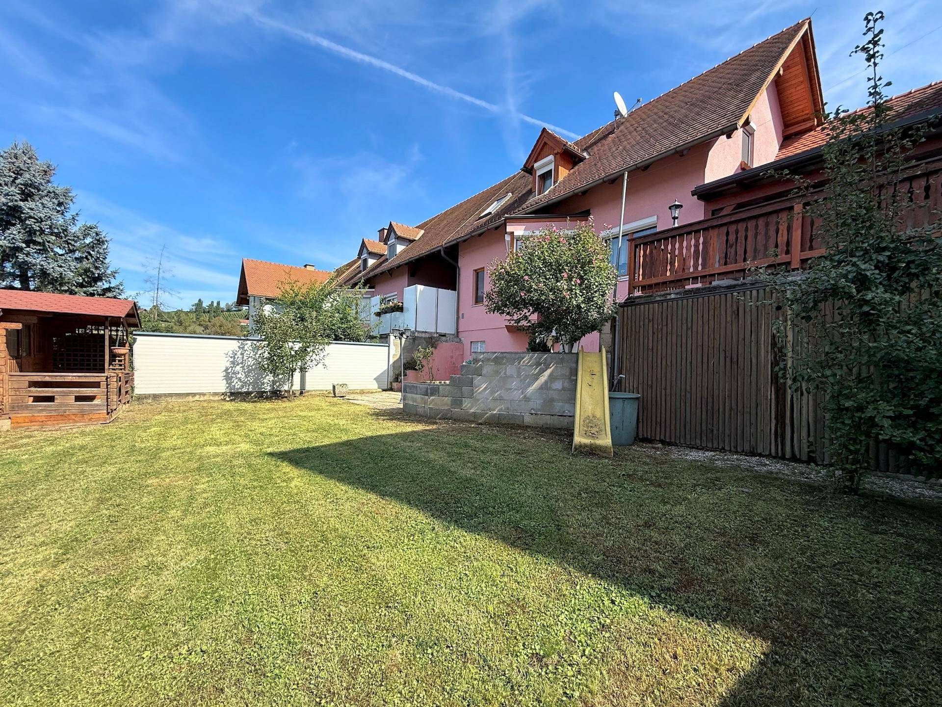 Großer Garten mit Rasenfläche, Kinderrutsche und Blick auf die Hausfassade.