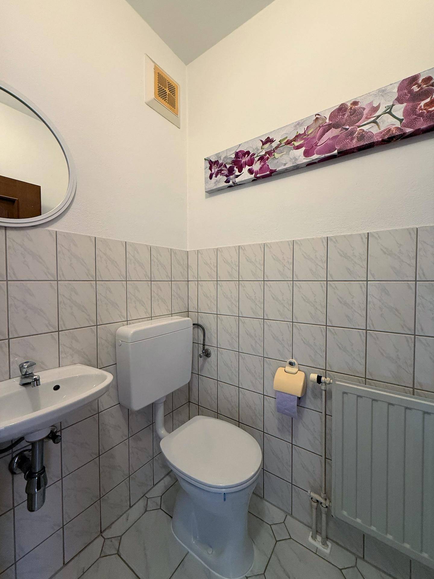 Kleines Gäste-WC mit weißen Fliesen, Waschbecken und Heizkörper.