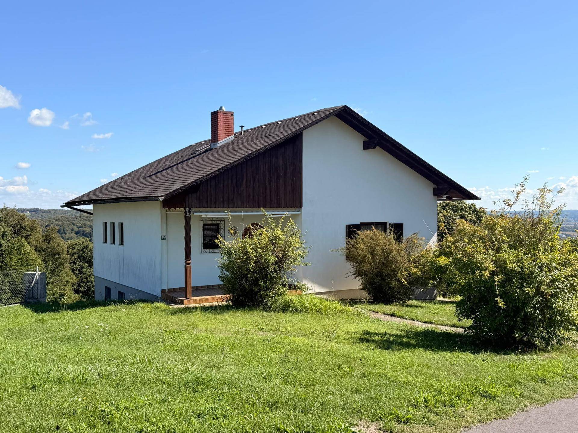 Einfamilienhaus in Hanglage mit weitem Blick und umgeben von grüner Natur unter blauem Himmel.
