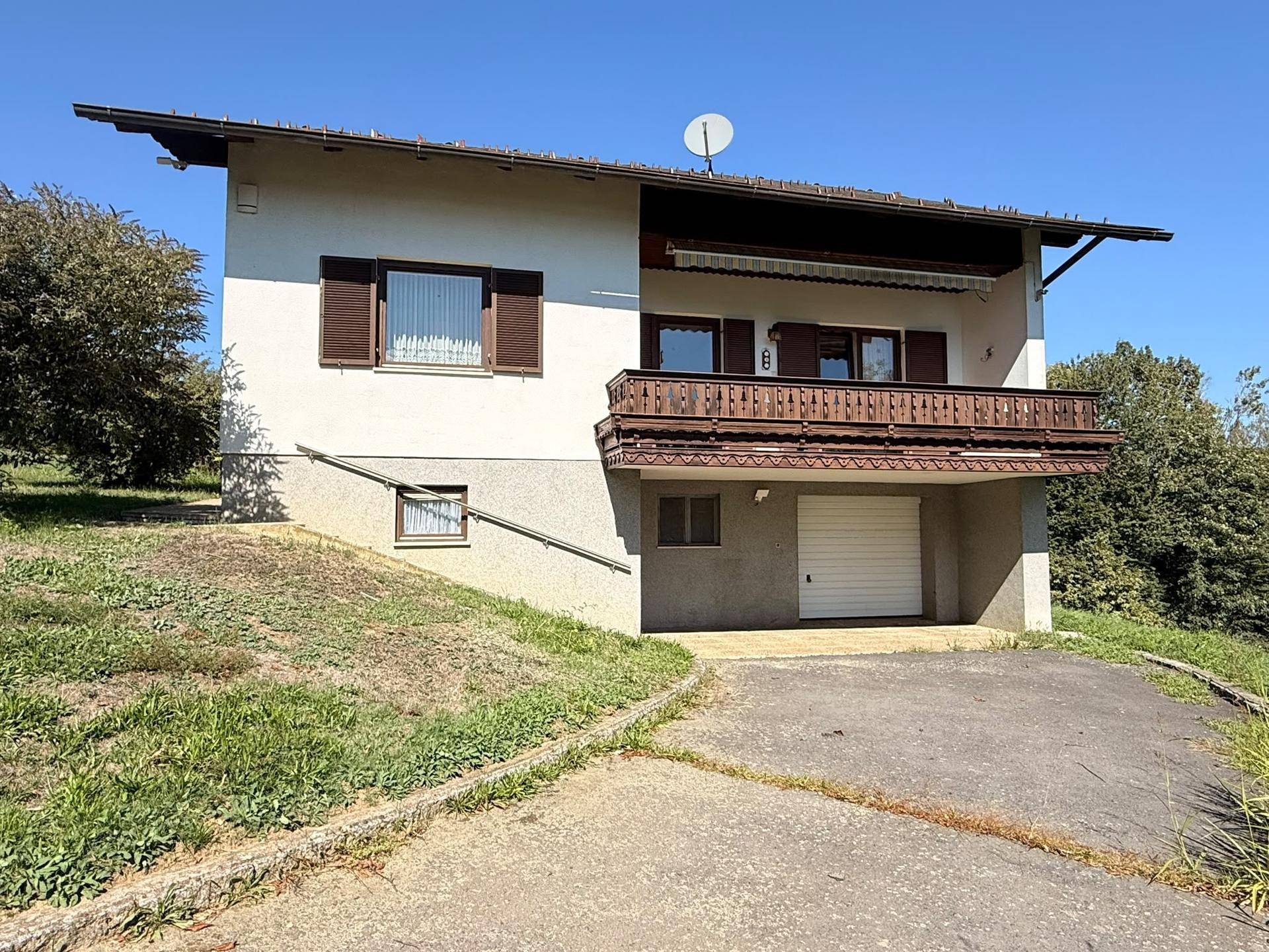 Rückseite des Hauses mit Balkon, integrierter Garage und Zufahrt auf dem Grundstück.
