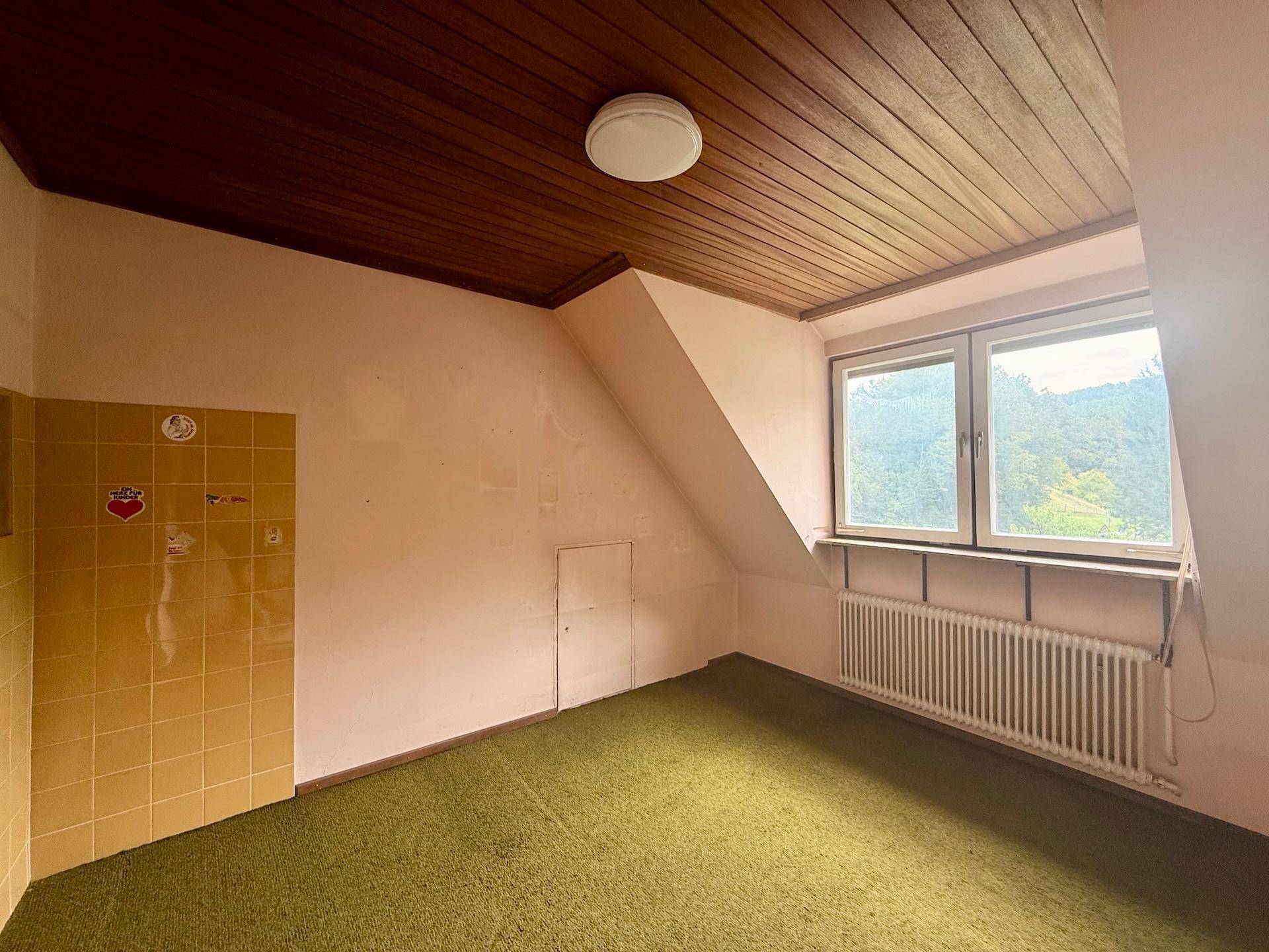 Dachzimmer mit Holzdecke, Teppichboden und Fenster, bietet einen gemütlichen Rückzugsort.