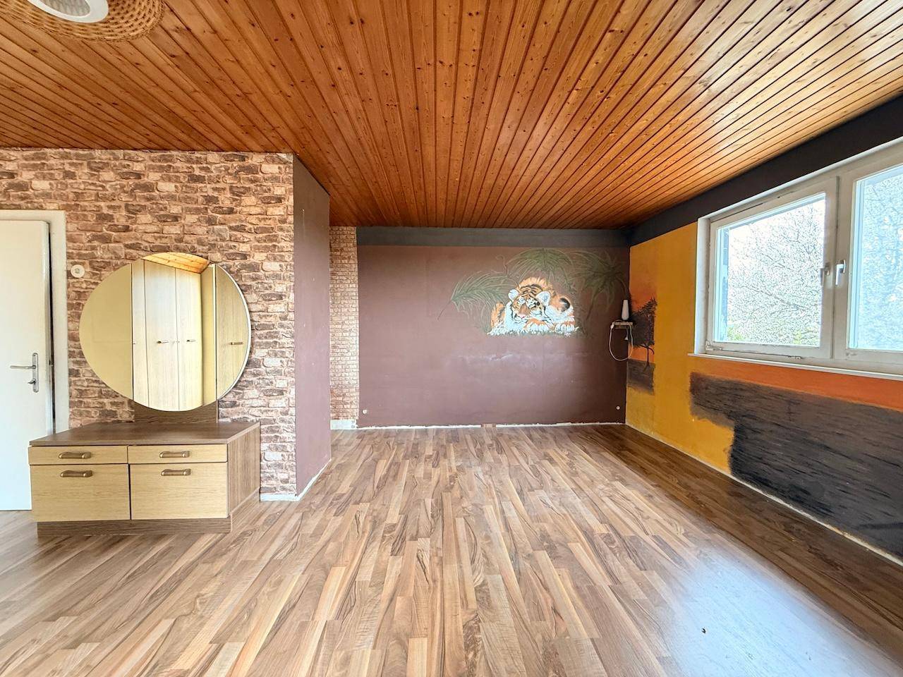 Zimmer mit Holzdecke, Laminatboden und dekorativer Wandgestaltung, bietet viel Platz.