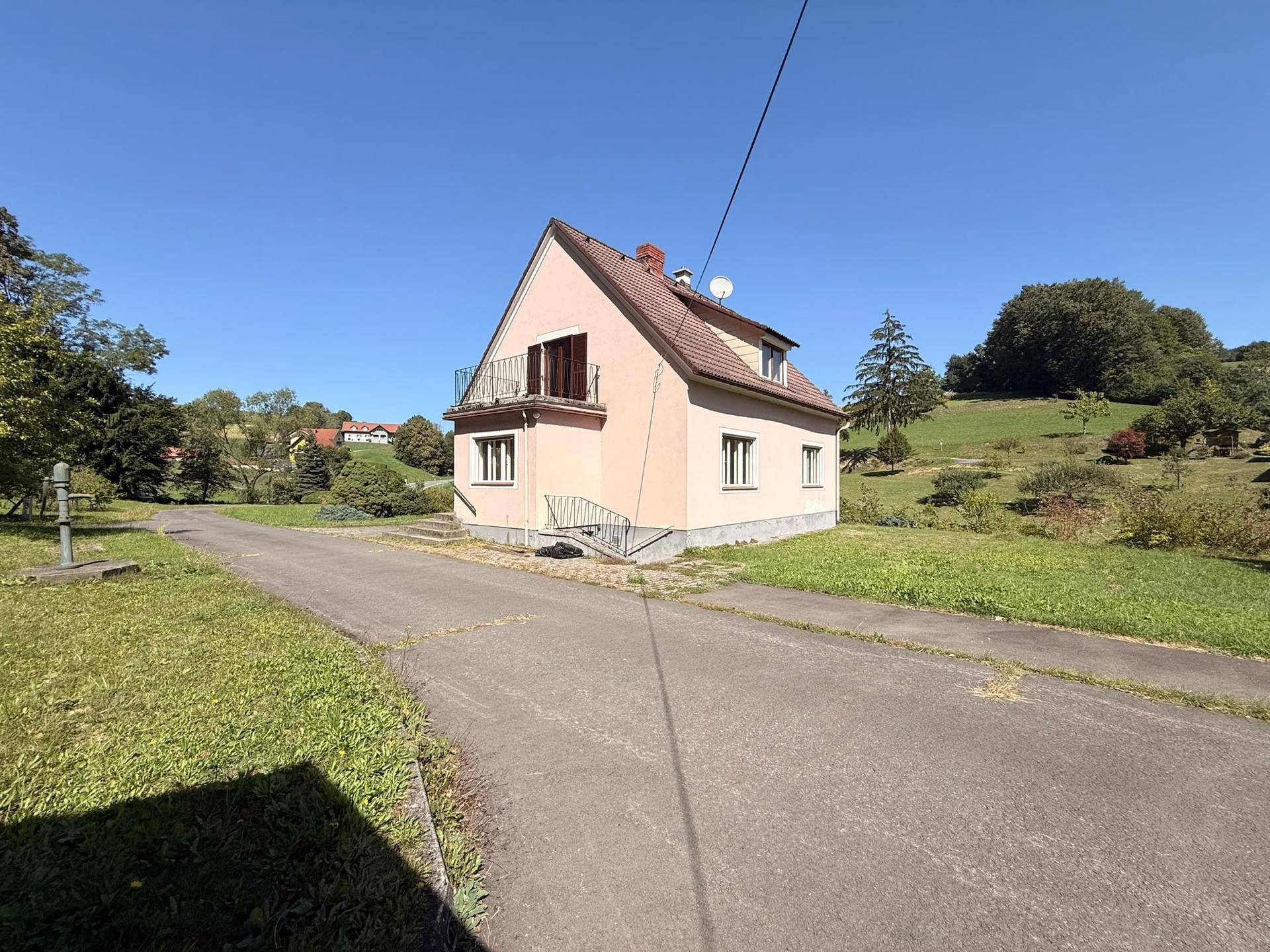 Freistehendes Haus mit Balkon und Zufahrt, eingebettet in eine idyllische, grüne Landschaft.