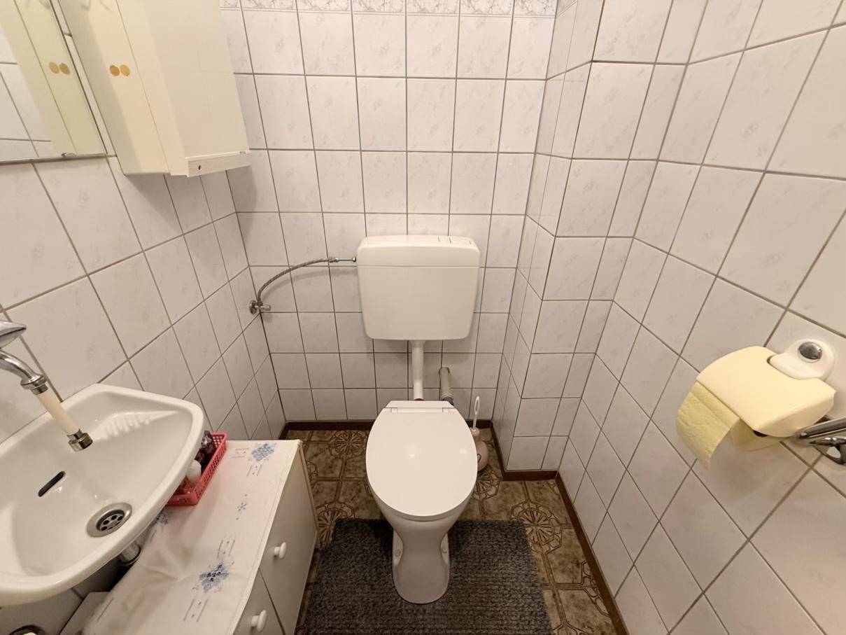 Kleines Gäste-WC mit Toilette, Waschbecken und weißen Fliesen an den Wänden.