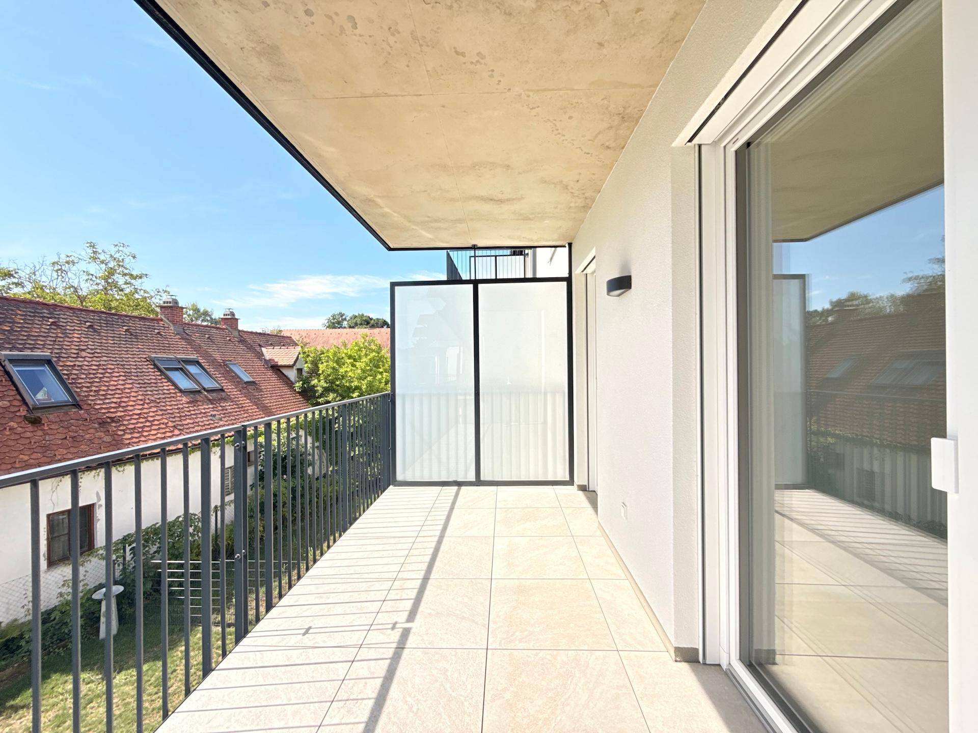 Großer Balkon mit Fliesenboden und Metallgeländer, bietet Blick auf die Umgebung.
