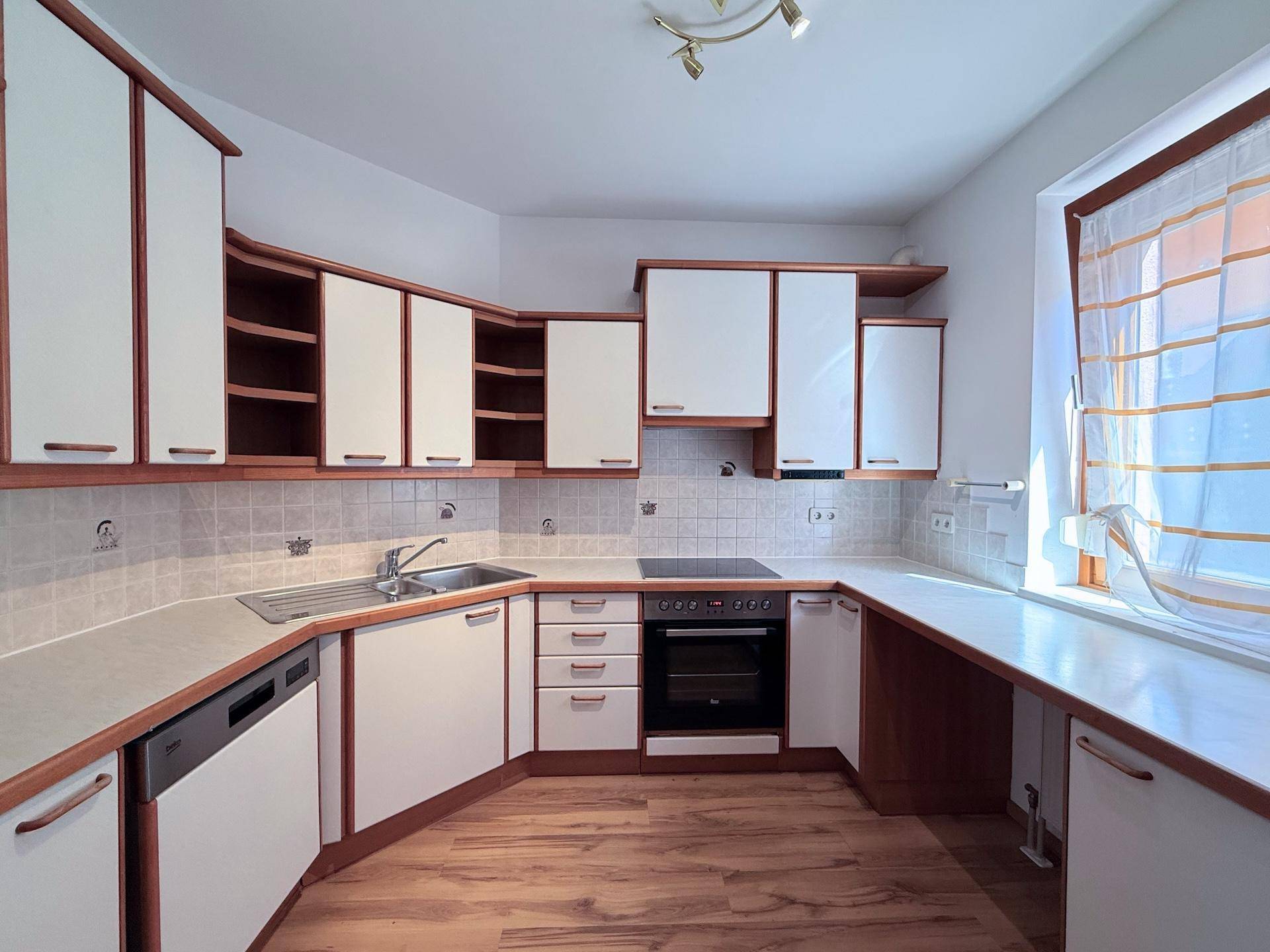 Funktionale Küche mit weißen und holzfarbenen Schränken, Fliesenrückwand und Fenster.