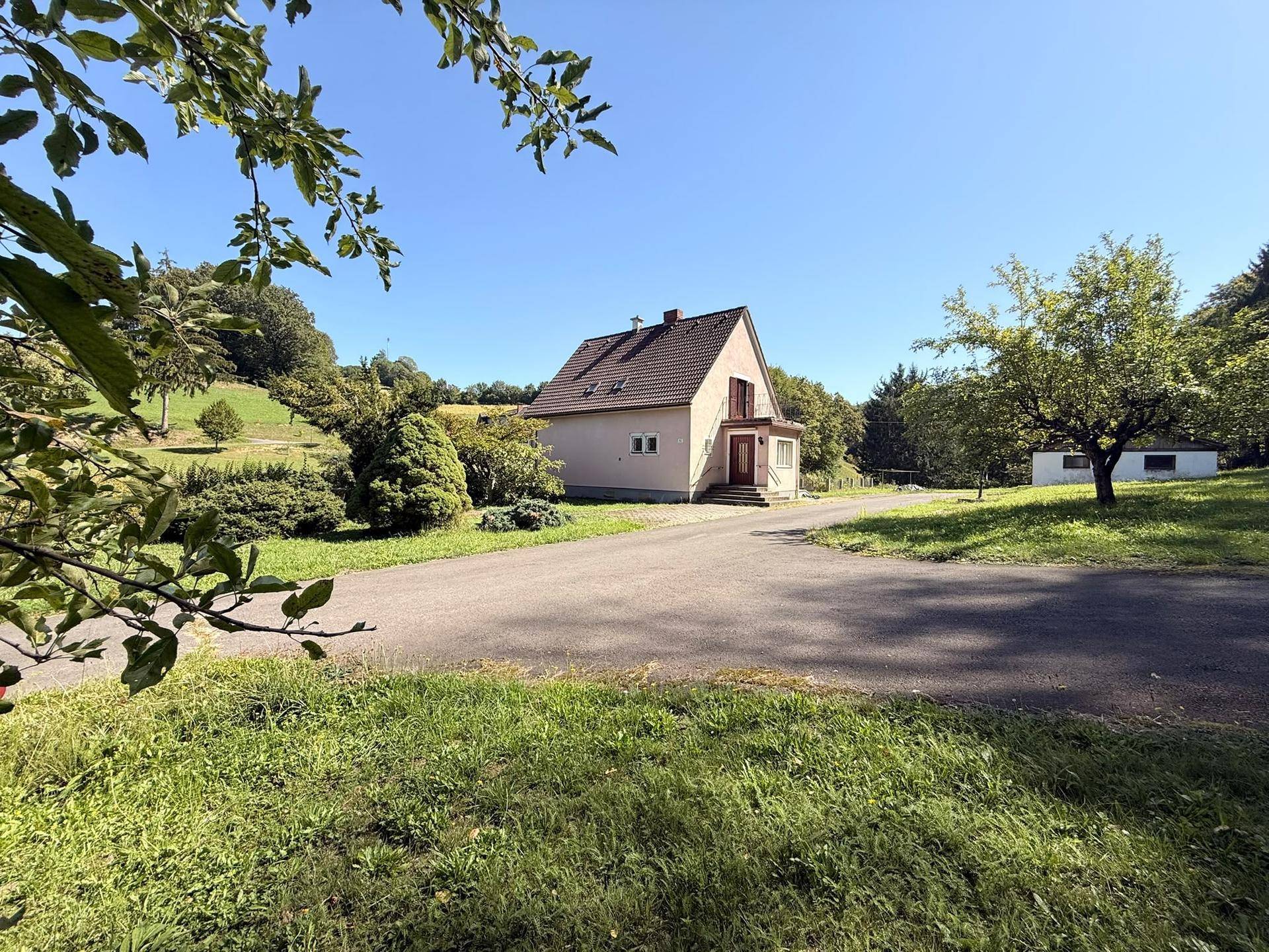 Einfamilienhaus mit großem Grundstück und Zufahrt, umgeben von Bäumen und grünen Wiesen.