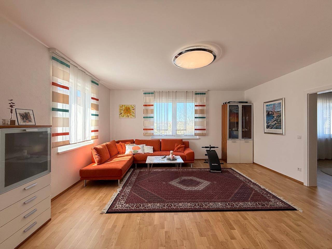Geräumiges Wohnzimmer mit Parkettboden, orangefarbenem Sofa und großen Fenstern für viel Licht.