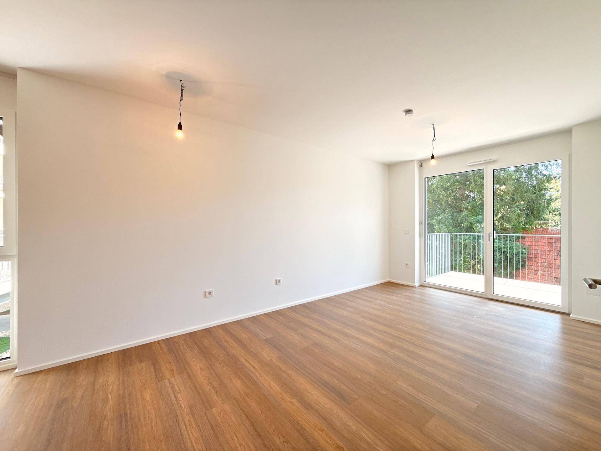 Geräumiges Wohnzimmer mit Laminatboden und großen Fenstern zum Balkon.