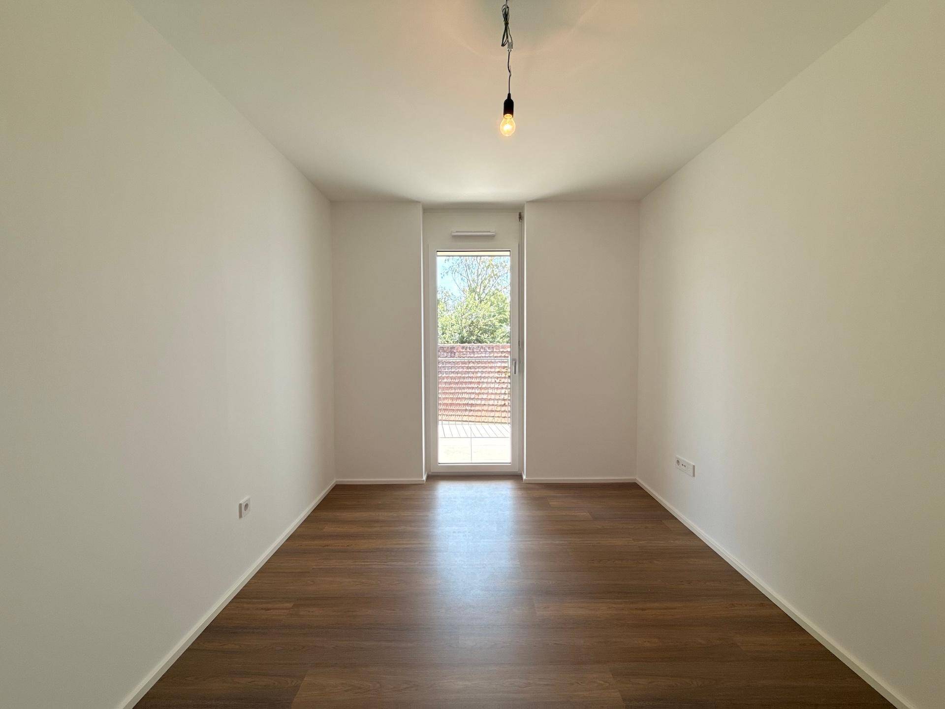 Helles Zimmer mit Holzboden und Balkontür, bereit für die individuelle Einrichtung.