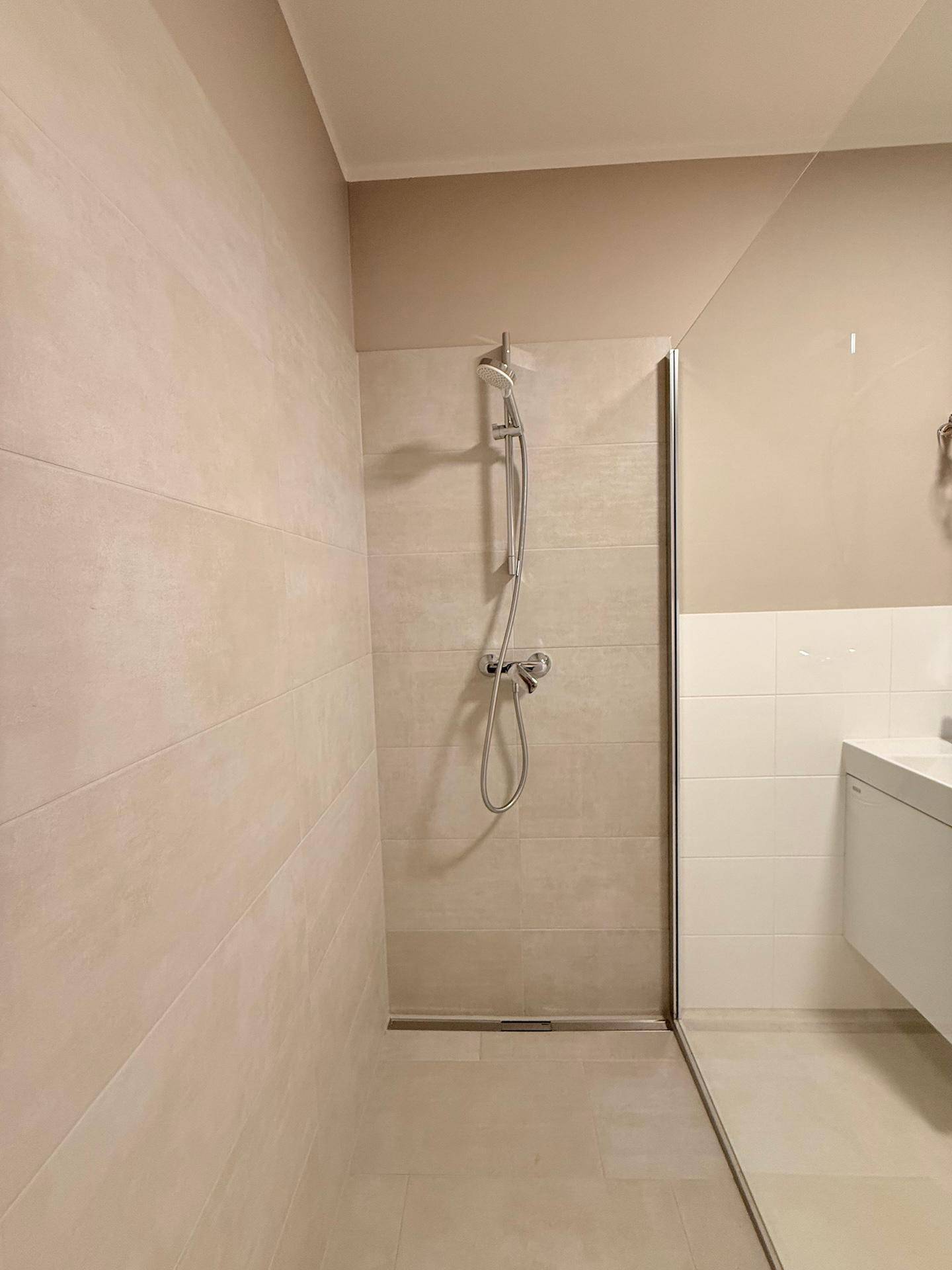 Ebenerdige Dusche mit Glaswand in einem modern gefliesten Badezimmer.