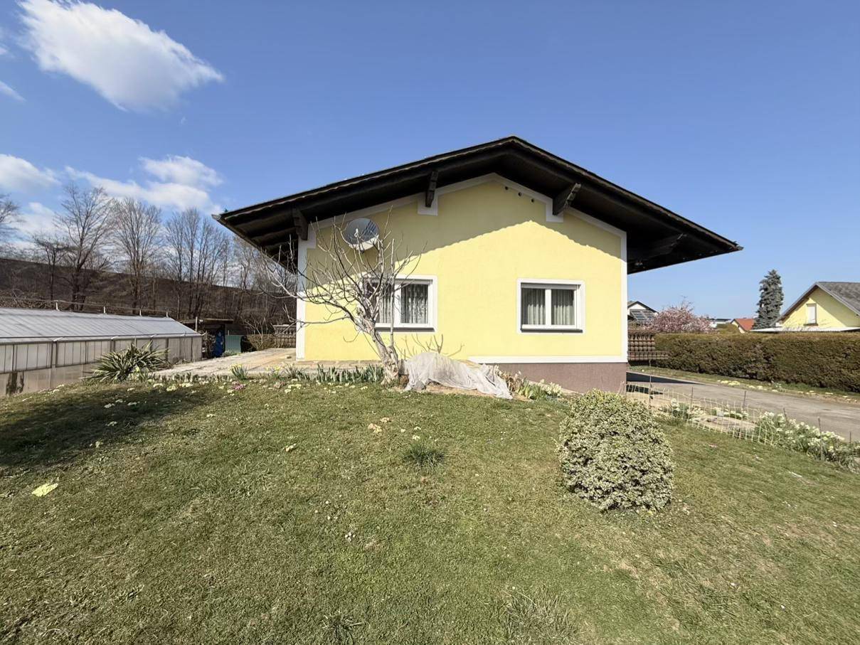 Ansicht des gelben Einfamilienhauses von der Seite mit einem grünen Rasenhügel und klarem Himmel.