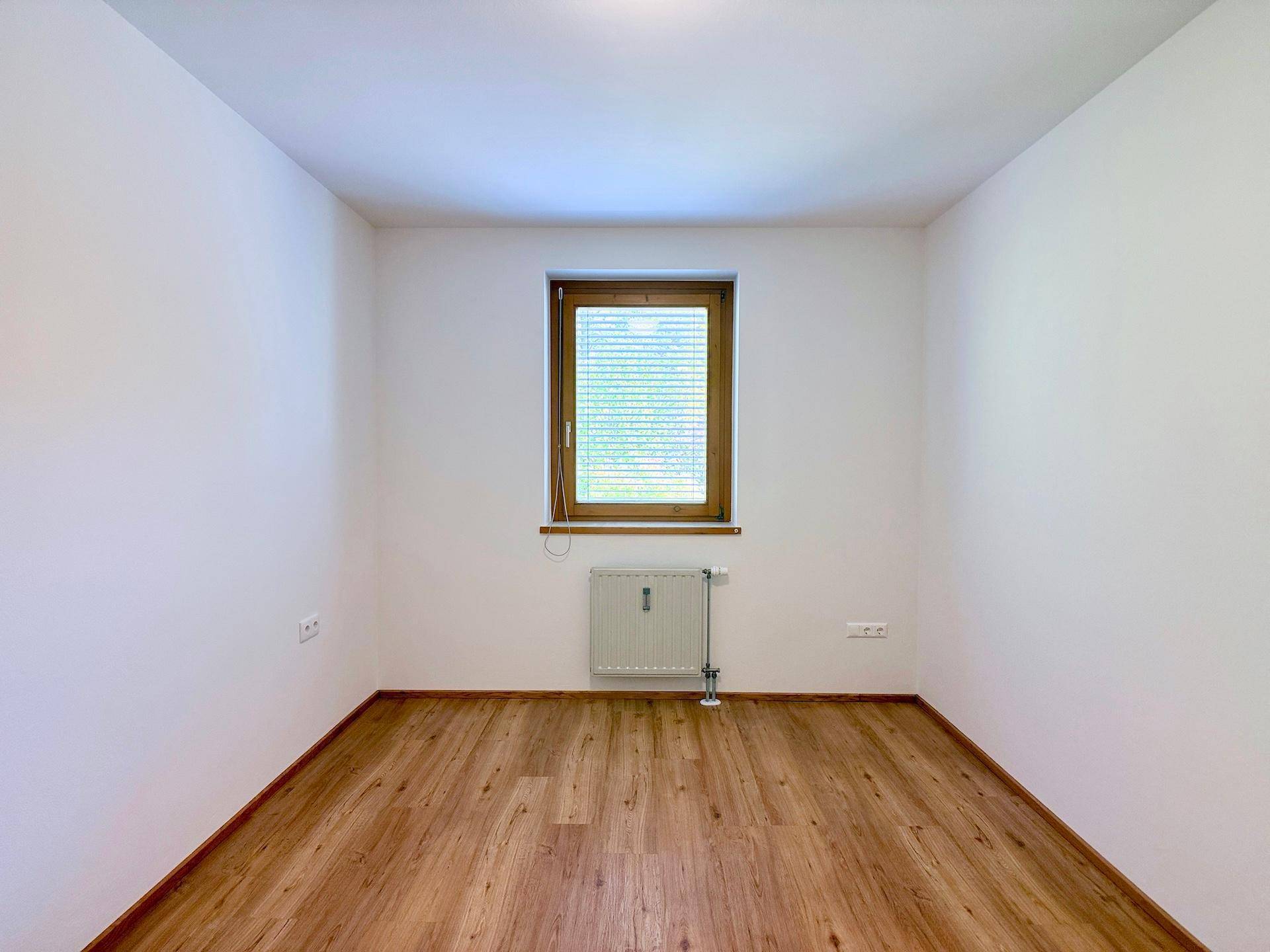 Helles Schlafzimmer mit Laminatboden und einem Fenster, das für angenehmes Tageslicht sorgt.