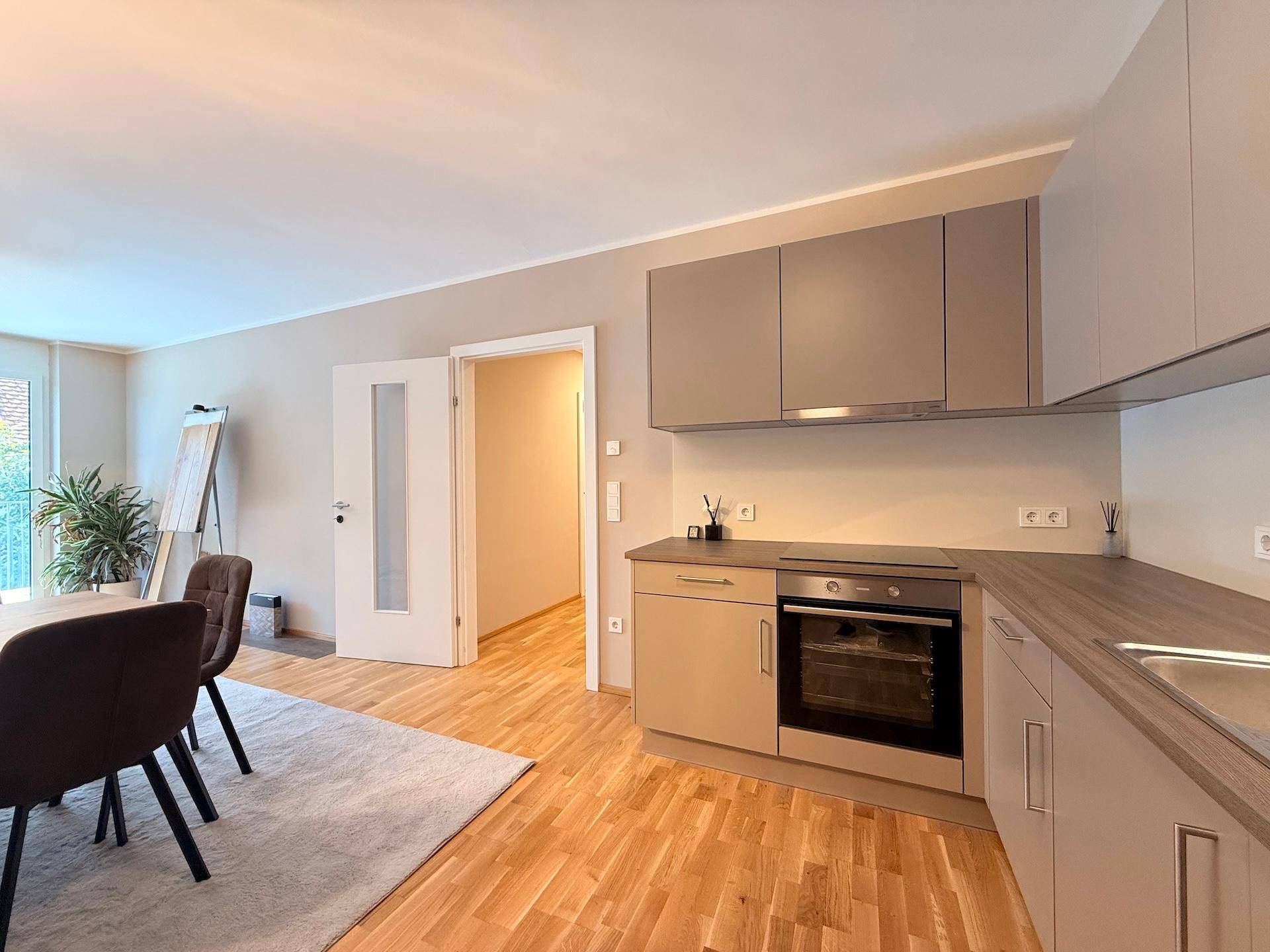 Moderne Küche mit hellen Schränken, Backofen und Blick in den angrenzenden Flur.