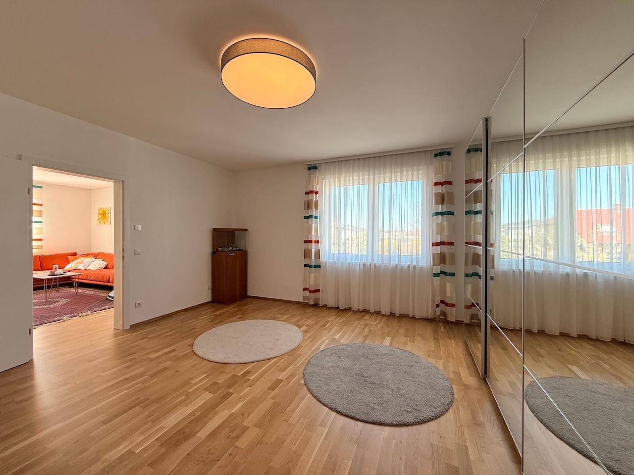 Helles Schlafzimmer mit Parkettboden, Spiegelschrank und großen Fenstern.