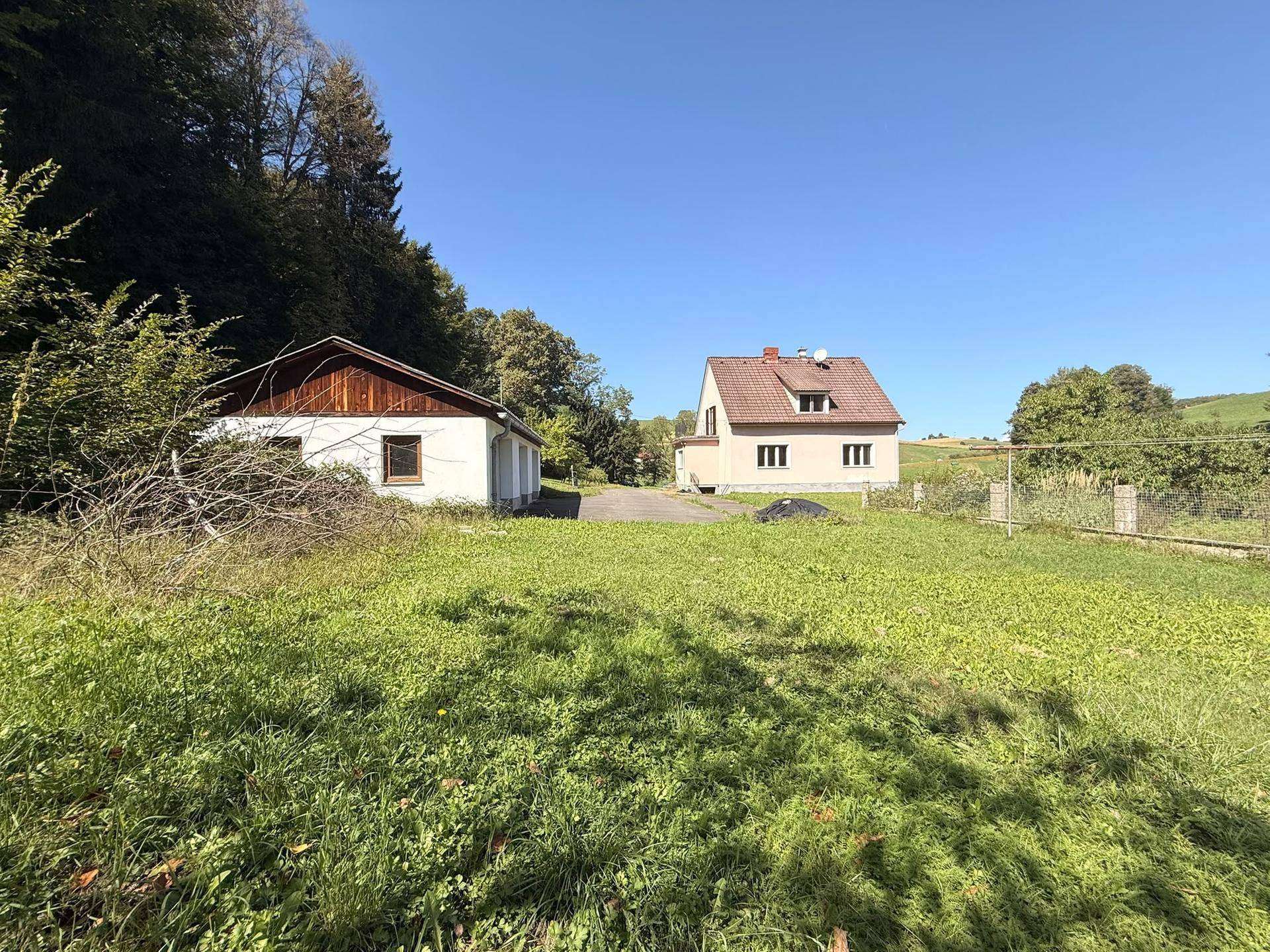 Weitläufiges Grundstück mit Einfamilienhaus und Nebengebäude, umgeben von grünen Wiesen.