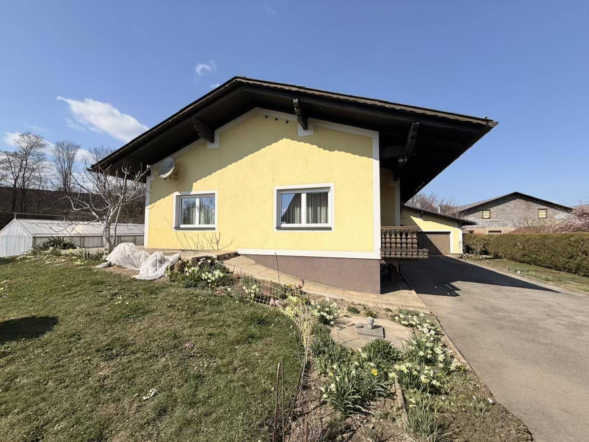 Seitenansicht des gelben Hauses mit blühenden Narzissen im Vorgarten unter blauem Himmel.