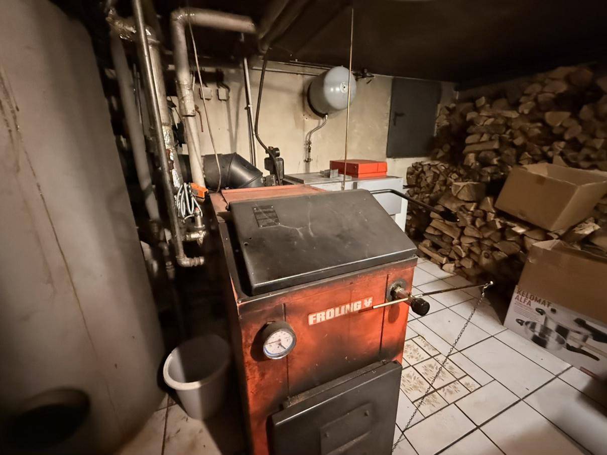 Heizraum mit Holzvergaserofen und gestapeltem Brennholz, typisch für eine ländliche Immobilie.