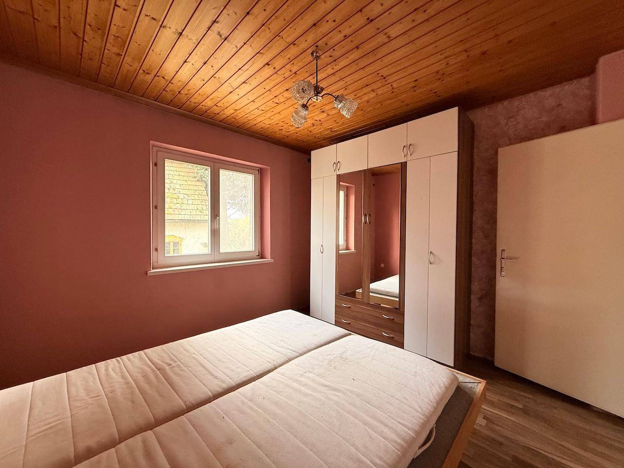 Schlafzimmer mit rosa Wänden, Holzdecke und großem Kleiderschrank, bietet viel Stauraum.