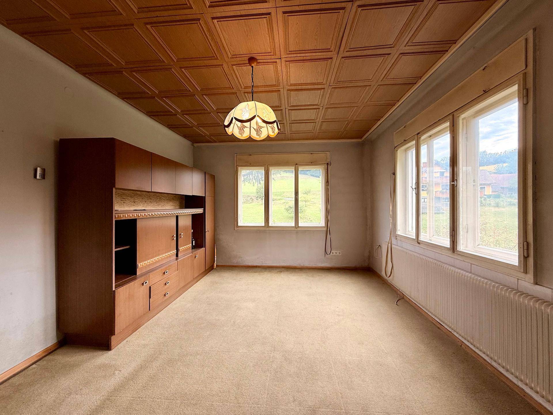 Helles Wohnzimmer mit Holzdecke, Teppichboden und Fenstern mit Blick auf die Landschaft.