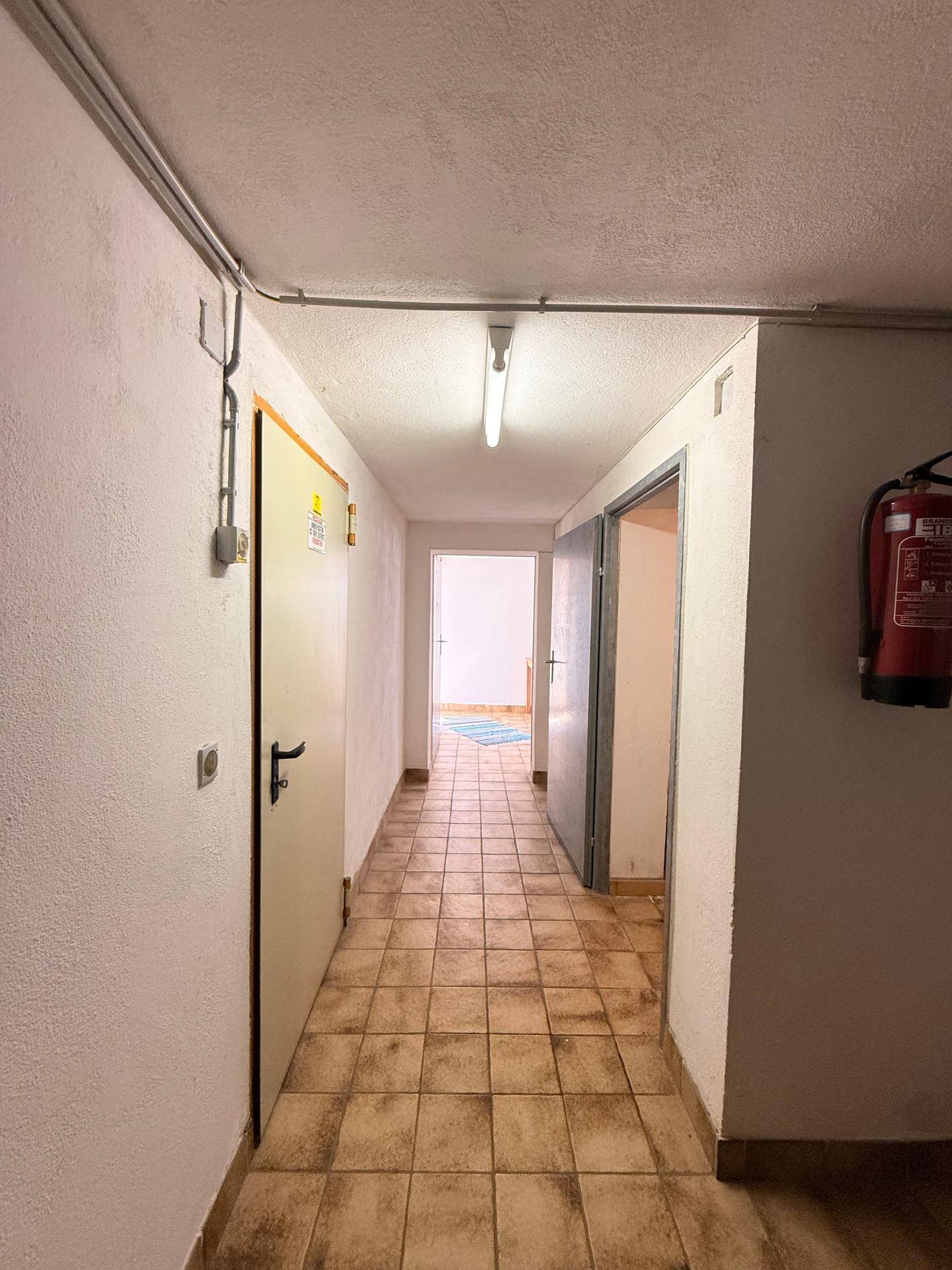 Kellerflur mit Fliesenboden und schlichten weißen Wänden, der zu verschiedenen Räumen führt.
