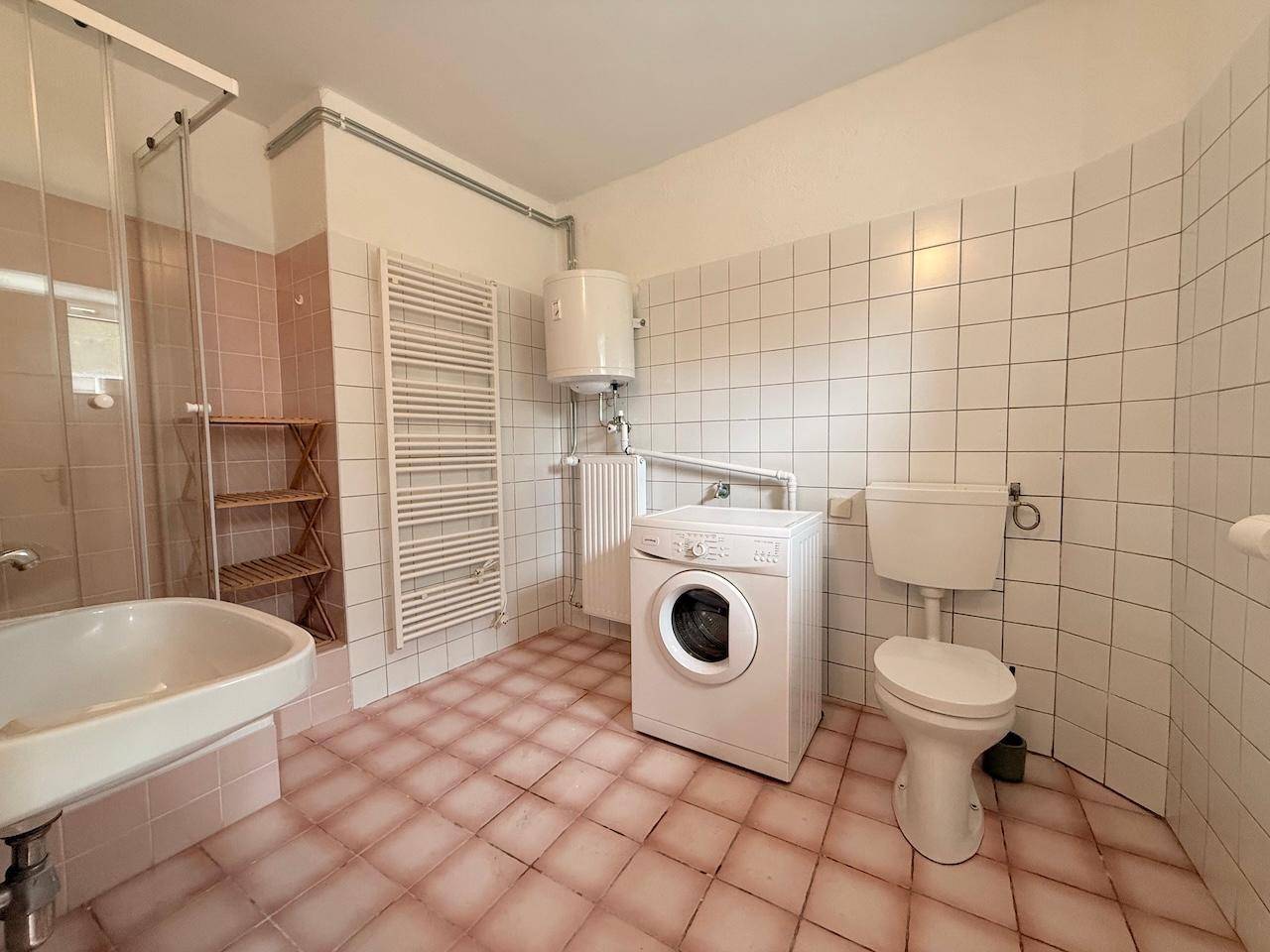Badezimmer mit Waschmaschine, Dusche und rosa-weißen Fliesen im 80er-Jahre-Stil.