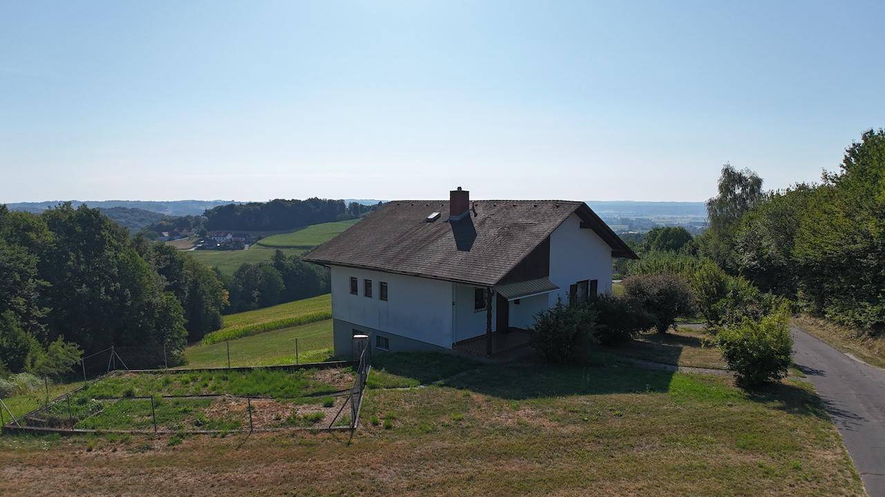 Panoramablick aus der Luft auf das Einfamilienhaus, eingebettet in eine grüne, hügelige Landschaft.