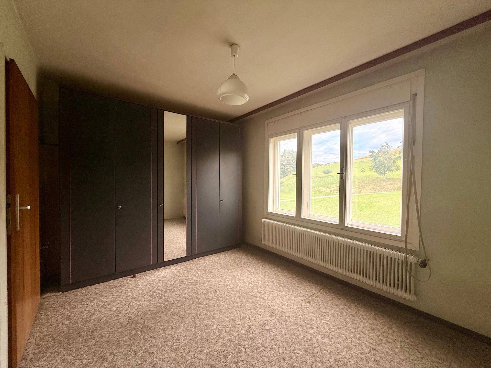 Schlafzimmer mit Teppichboden, großem Fenster und Einbauschrank, bietet viel Stauraum und Licht.