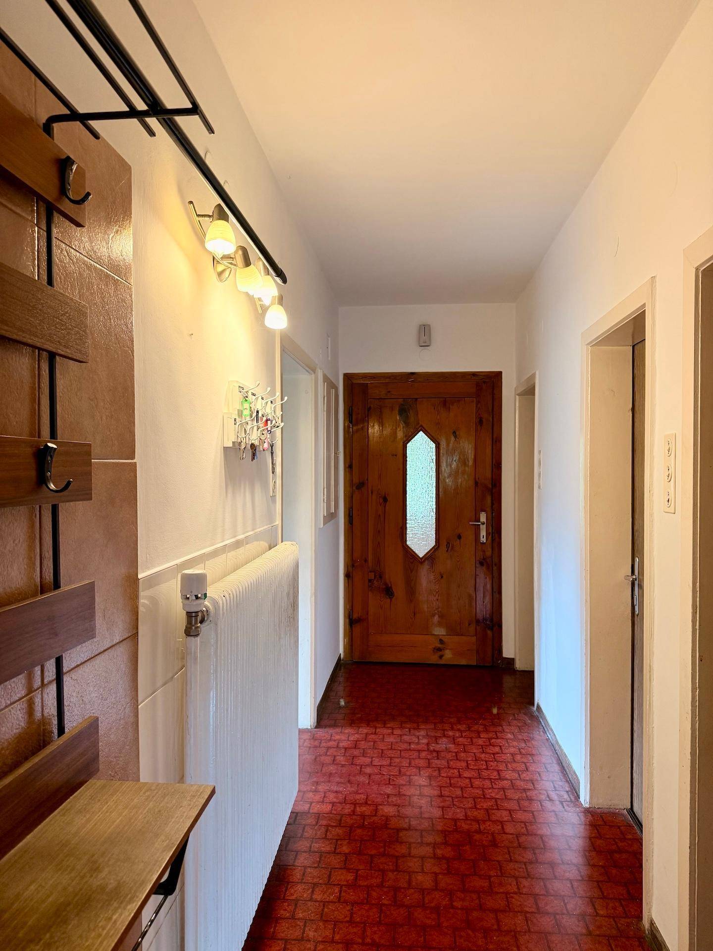 Flur mit rotem Fliesenboden, Garderobe und Holztür, bietet einen praktischen Eingangsbereich.