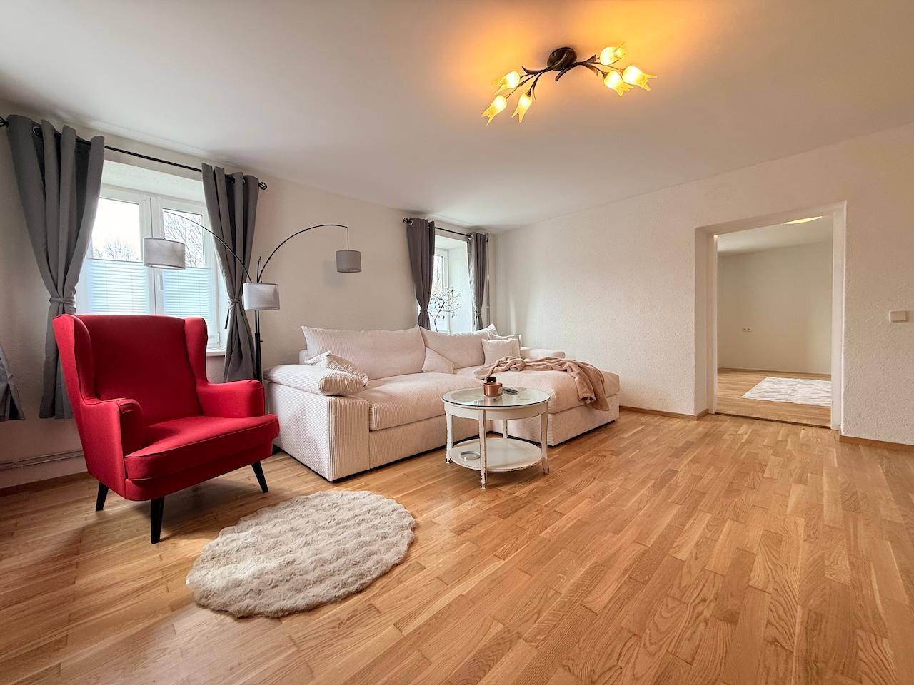 Helles Wohnzimmer mit bequemer Couch, rotem Sessel und Holzboden.