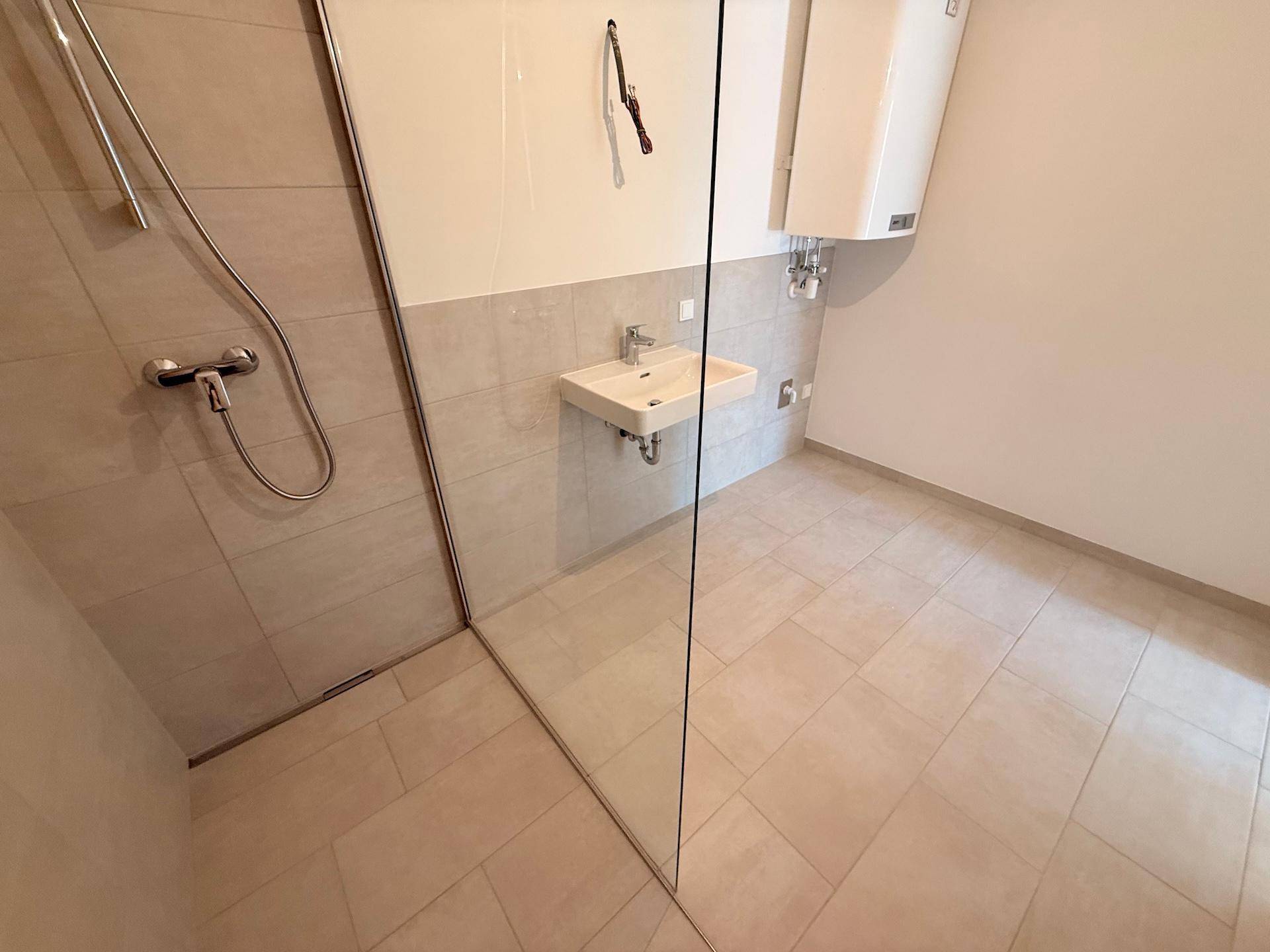 Blick auf den gefliesten Boden und die Glasabtrennung der begehbaren Dusche.