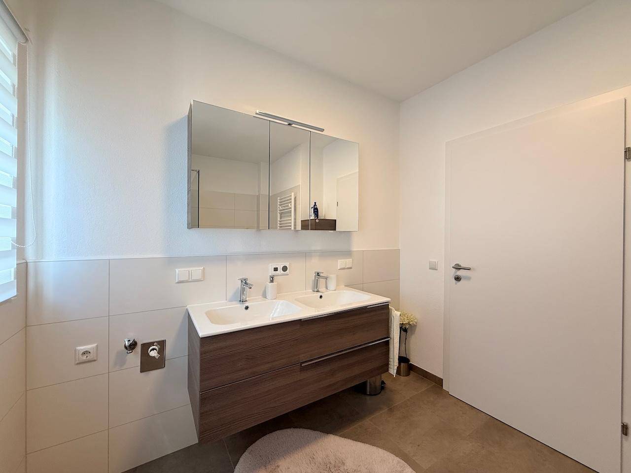 Badezimmer mit Doppelwaschbecken, Spiegelschrank und Fenster für Tageslicht.