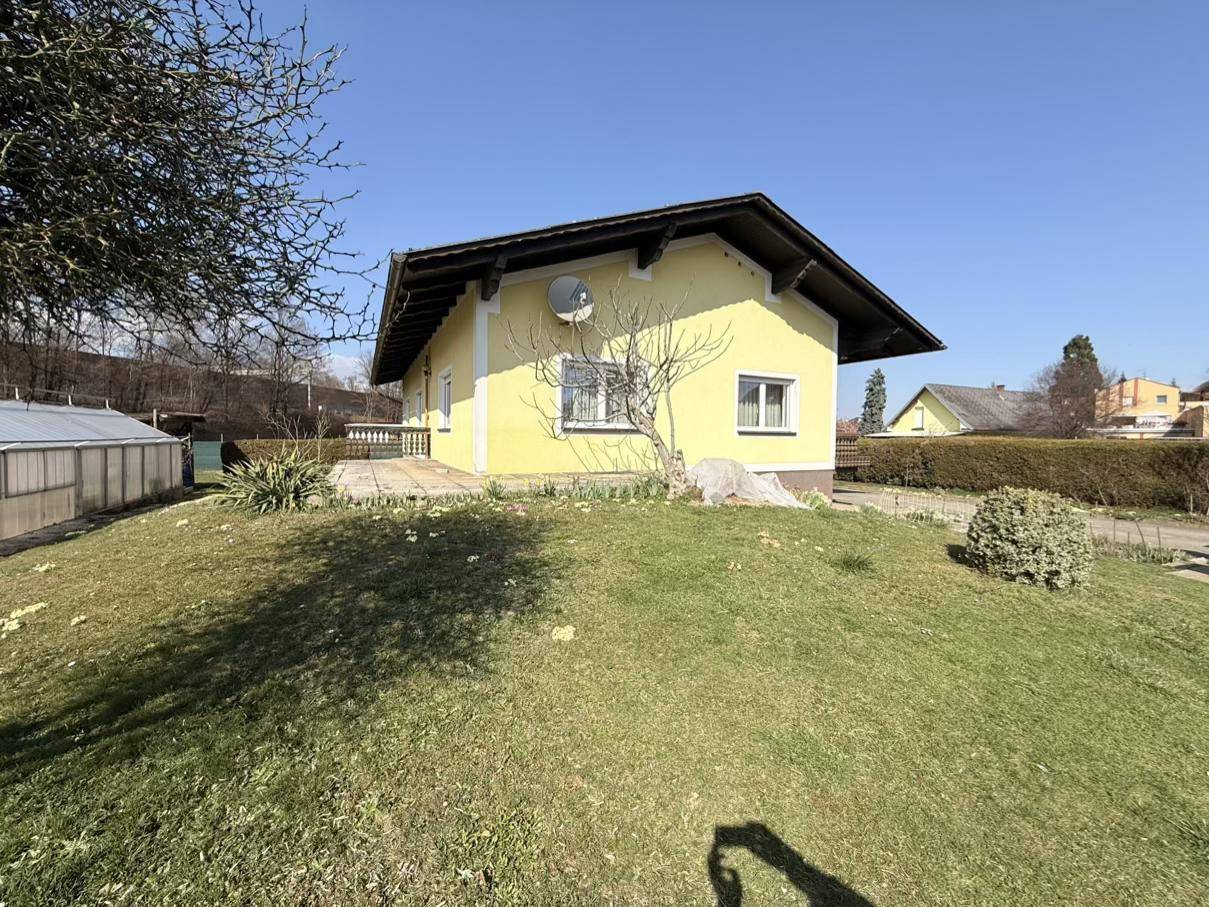 Ansicht des gelben Einfamilienhauses von der Seite mit einem grünen Rasenhügel und klarem Himmel.