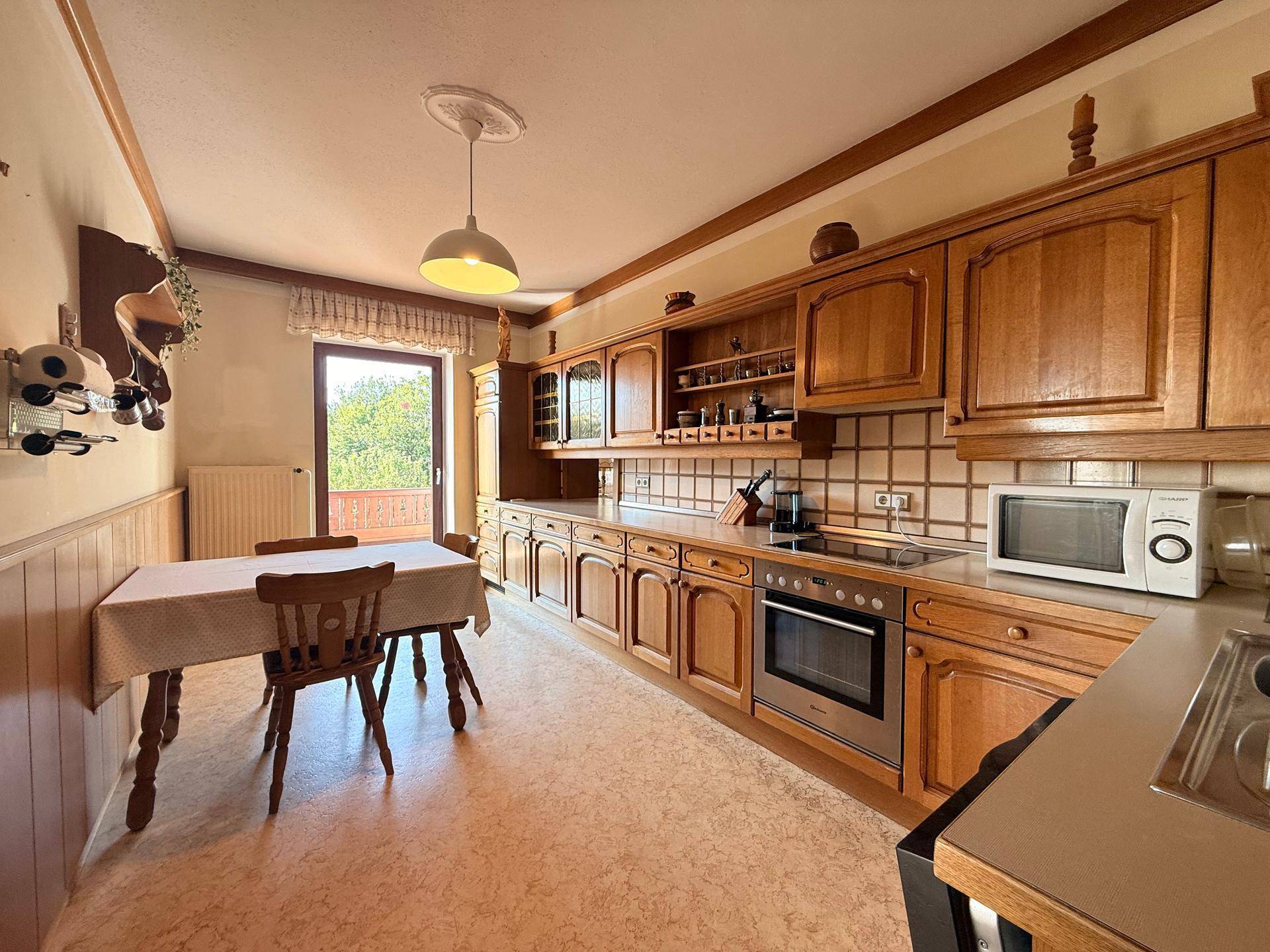 Gemütliche Küche mit Holzschränken, Essbereich und Zugang zu einem Balkon mit Ausblick.