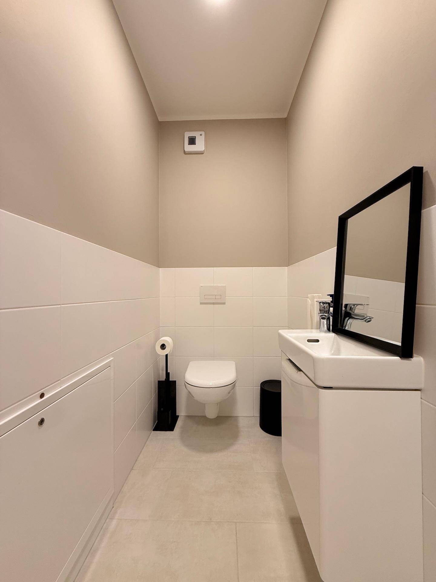 Modernes Gäste-WC mit wandhängendem WC, Waschbecken und Spiegel.