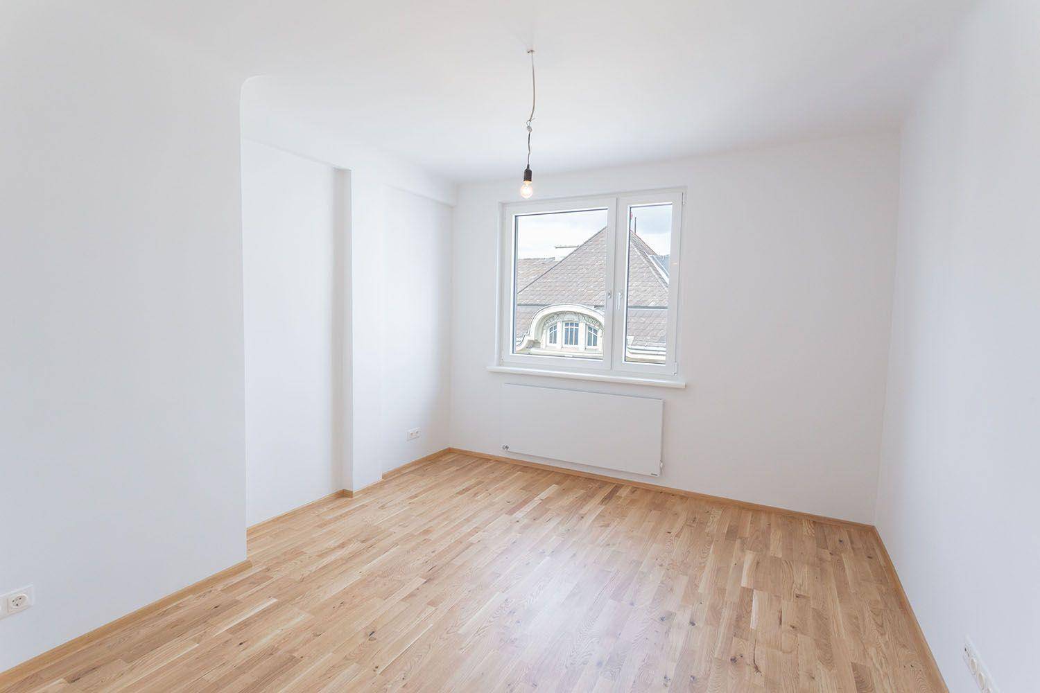 Helles Zimmer mit Parkettboden und großem Fenster, bietet Blick auf die Umgebung.