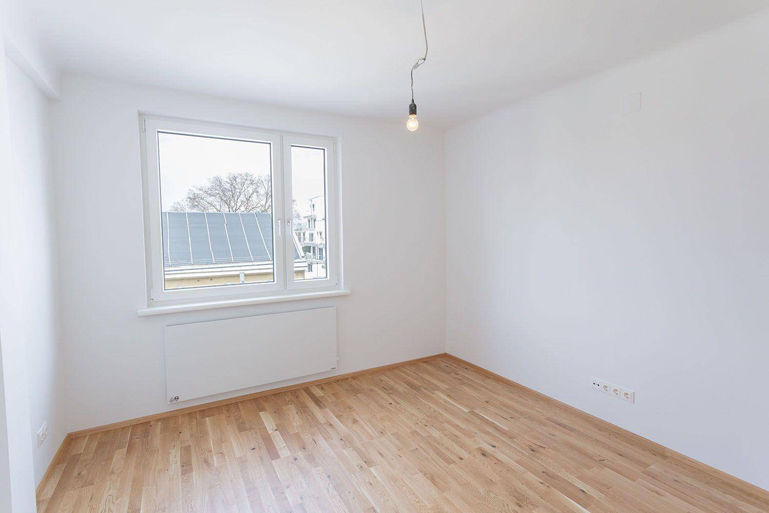 Lichtdurchflutetes Zimmer mit Holzboden und großem Fenster, ideal als Schlaf- oder Arbeitszimmer.