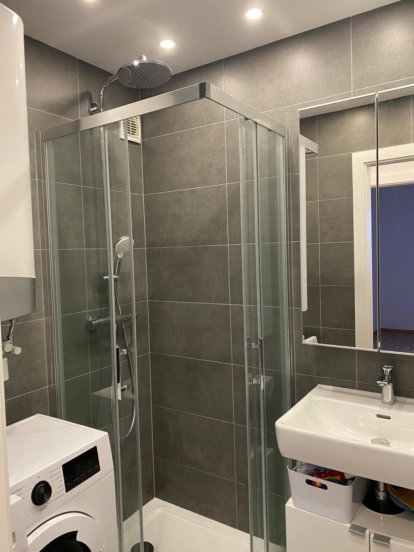 Modernes Badezimmer mit großer Duschkabine, Waschbecken und Waschmaschine.