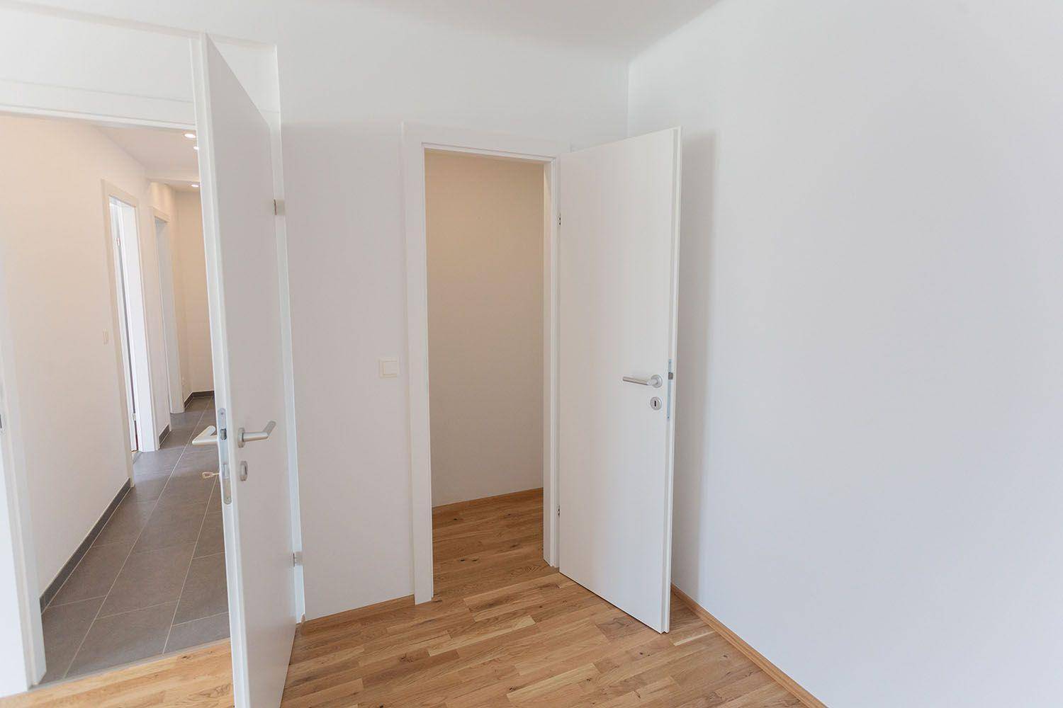 Helles Zimmer mit Parkettboden und zwei Türen, die zu anderen Bereichen führen.